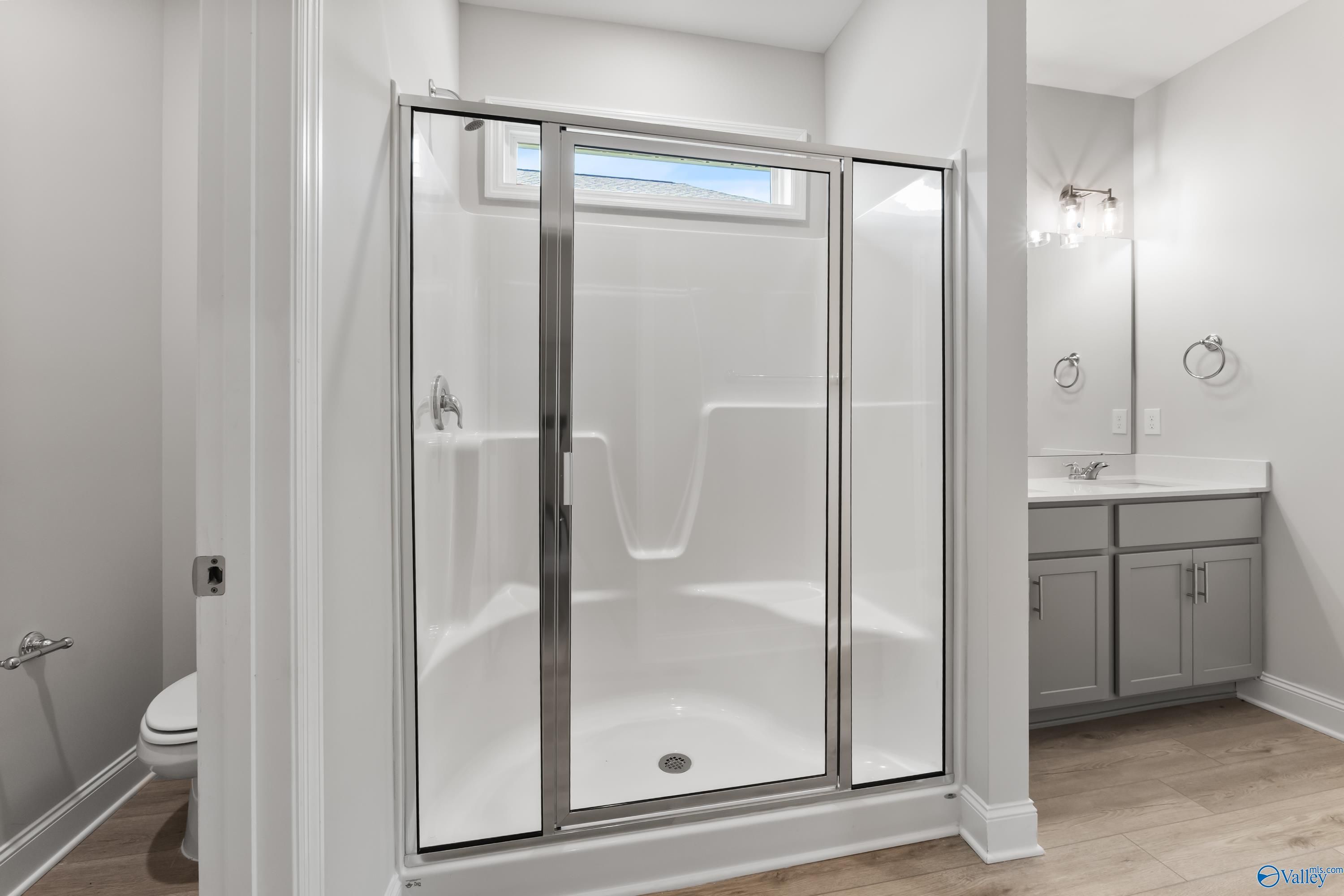 Modern bathroom with frameless glass shower, single vanity, and wood flooring in Davidson Homes The Daphne C, Huntsville AL