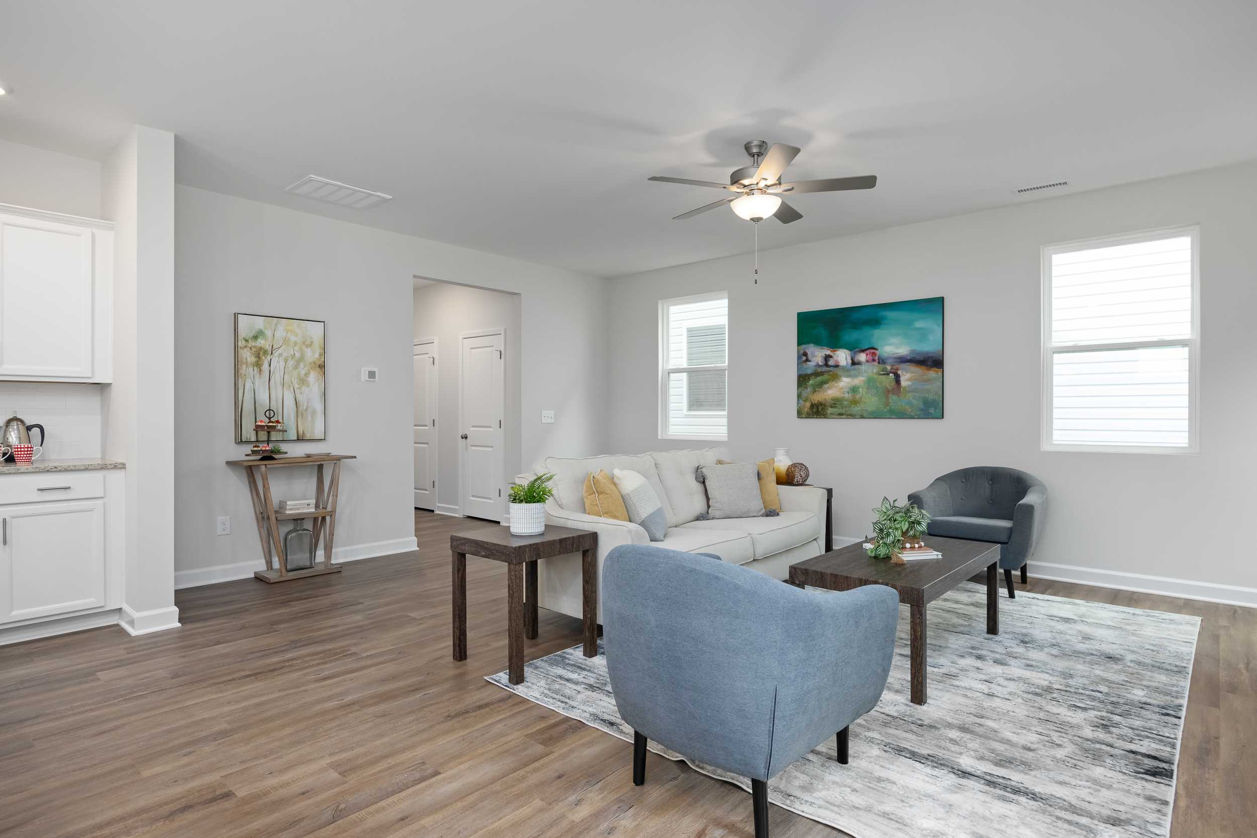 Spacious open-concept living room at Gregory Village Townhomes in Lillington NC with white sofa, blue armchair, hardwood floors, and modern artwork