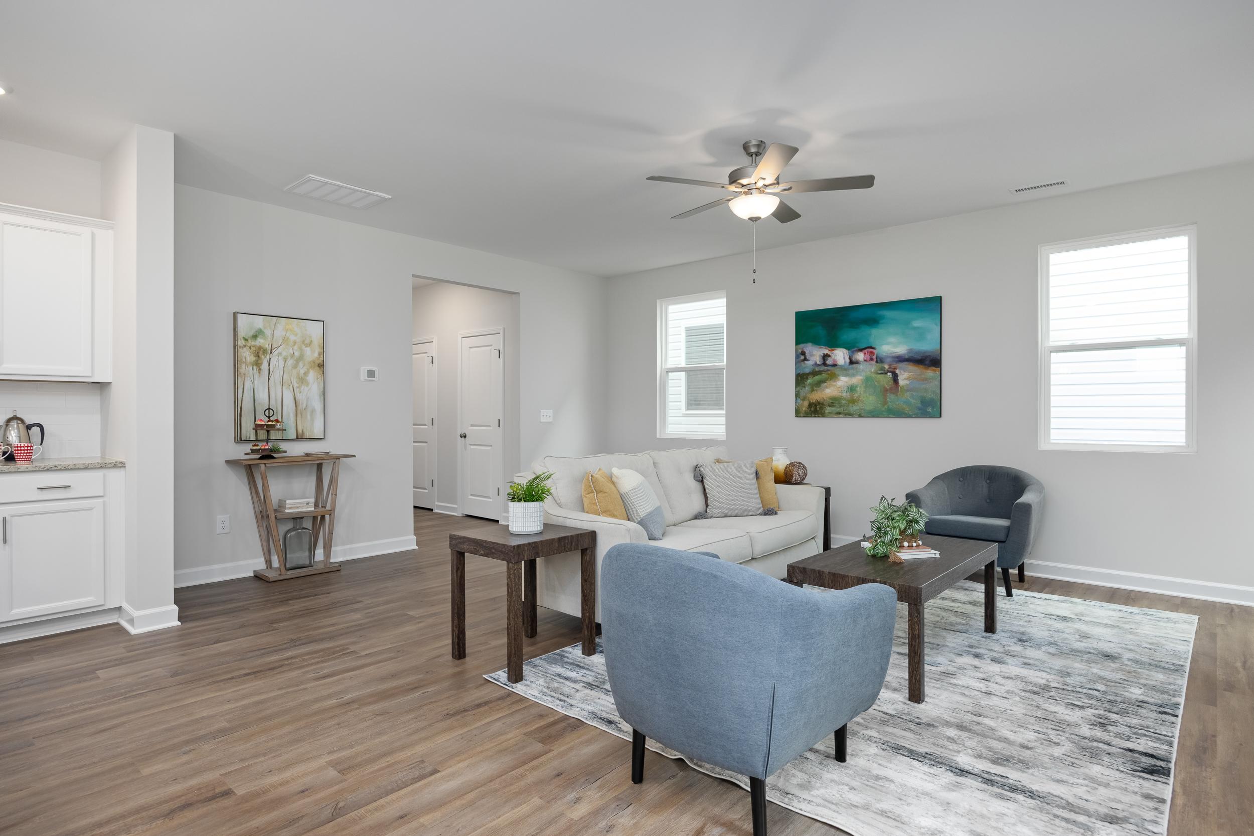 Spacious open-concept living room at Gregory Village Townhomes in Lillington NC with white sofa, blue armchair, hardwood floors, and modern artwork