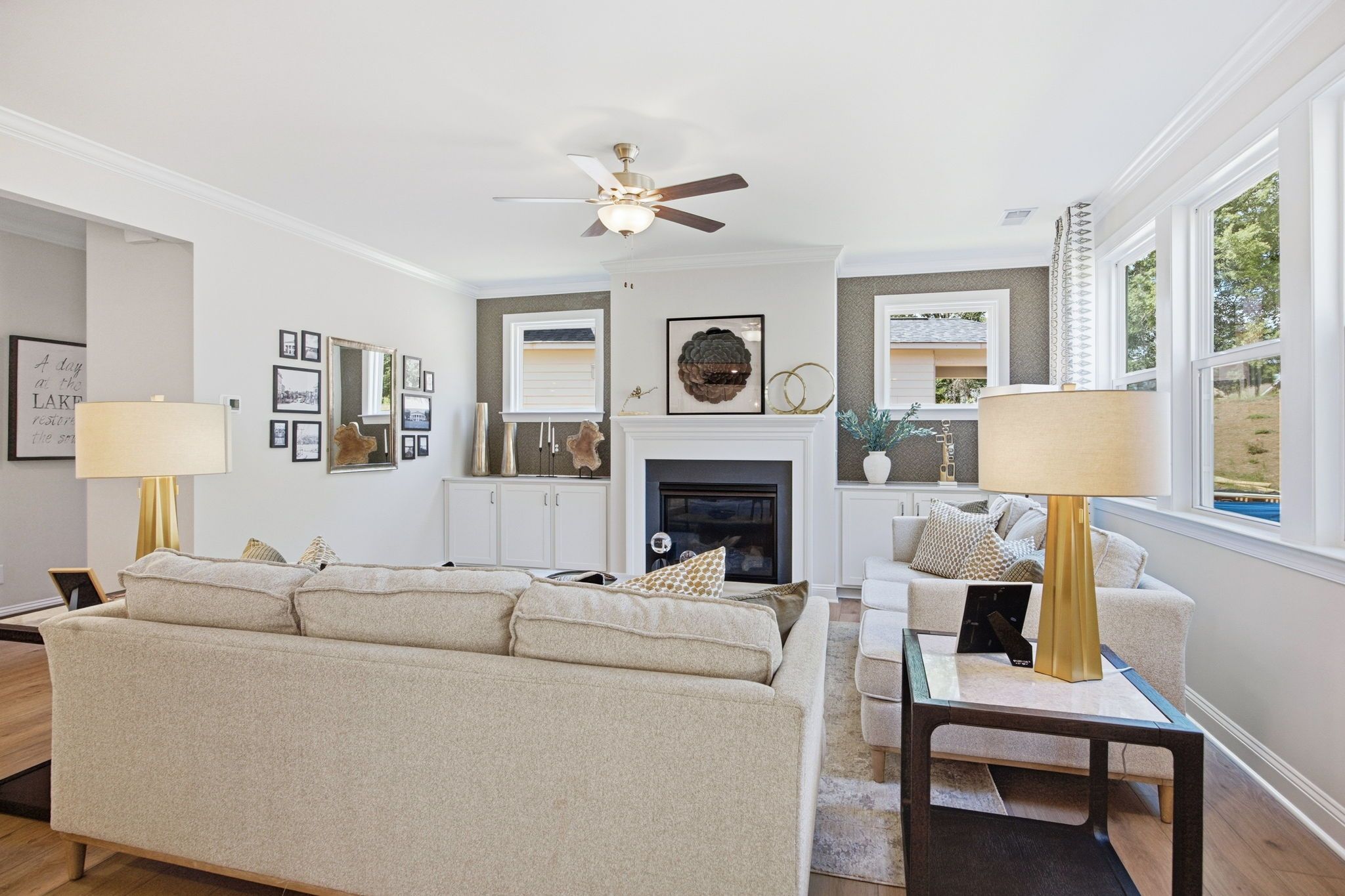 Spacious living room at Enclave at Belmont in Belmont NC with beige sectional sofa, white fireplace, gold lamps, and large windows