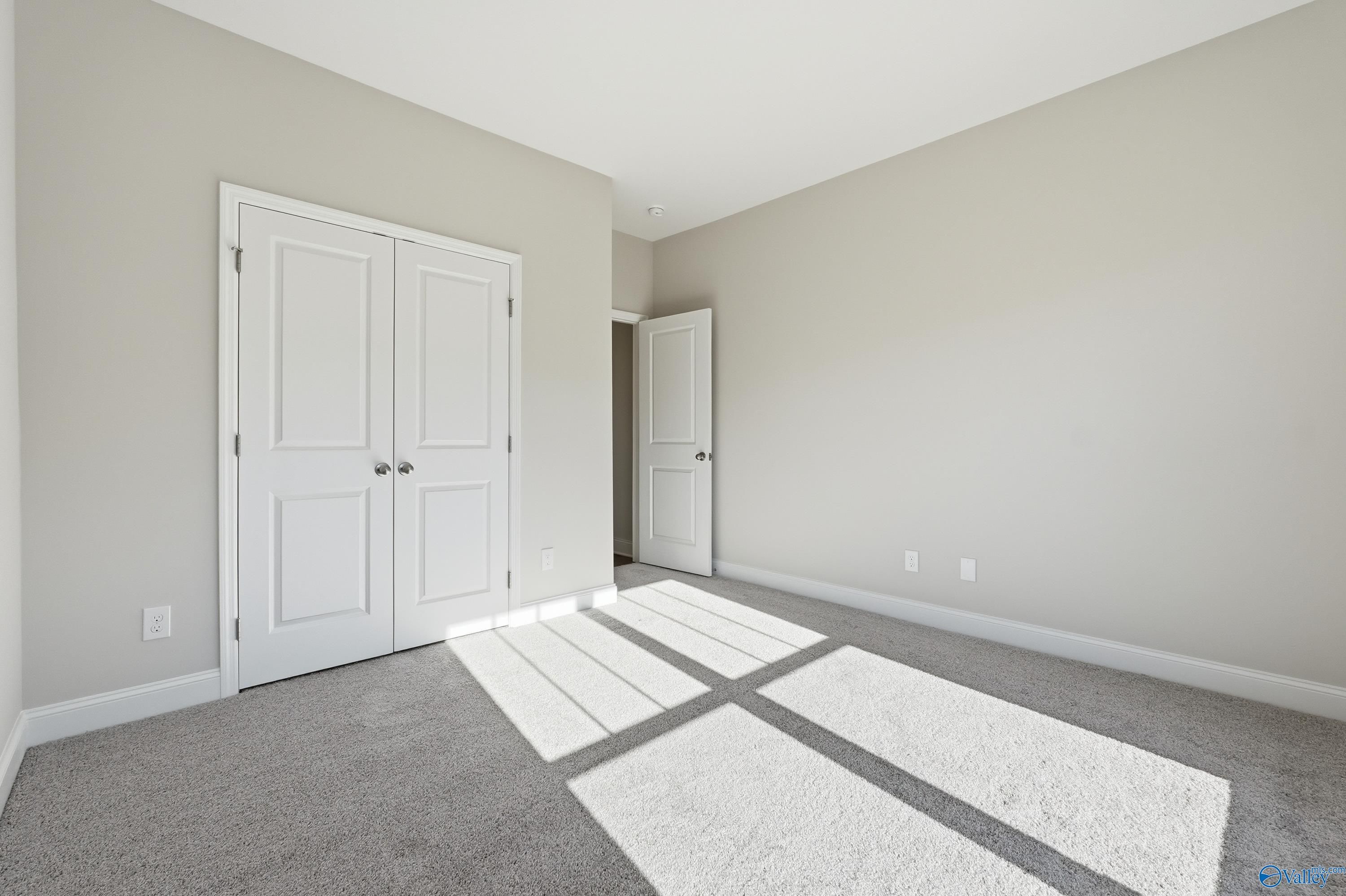 Bright bedroom featuring neutral walls, white double closet doors, carpet floor, and natural sunlight in Davidson Homes The Everett, Harvest AL