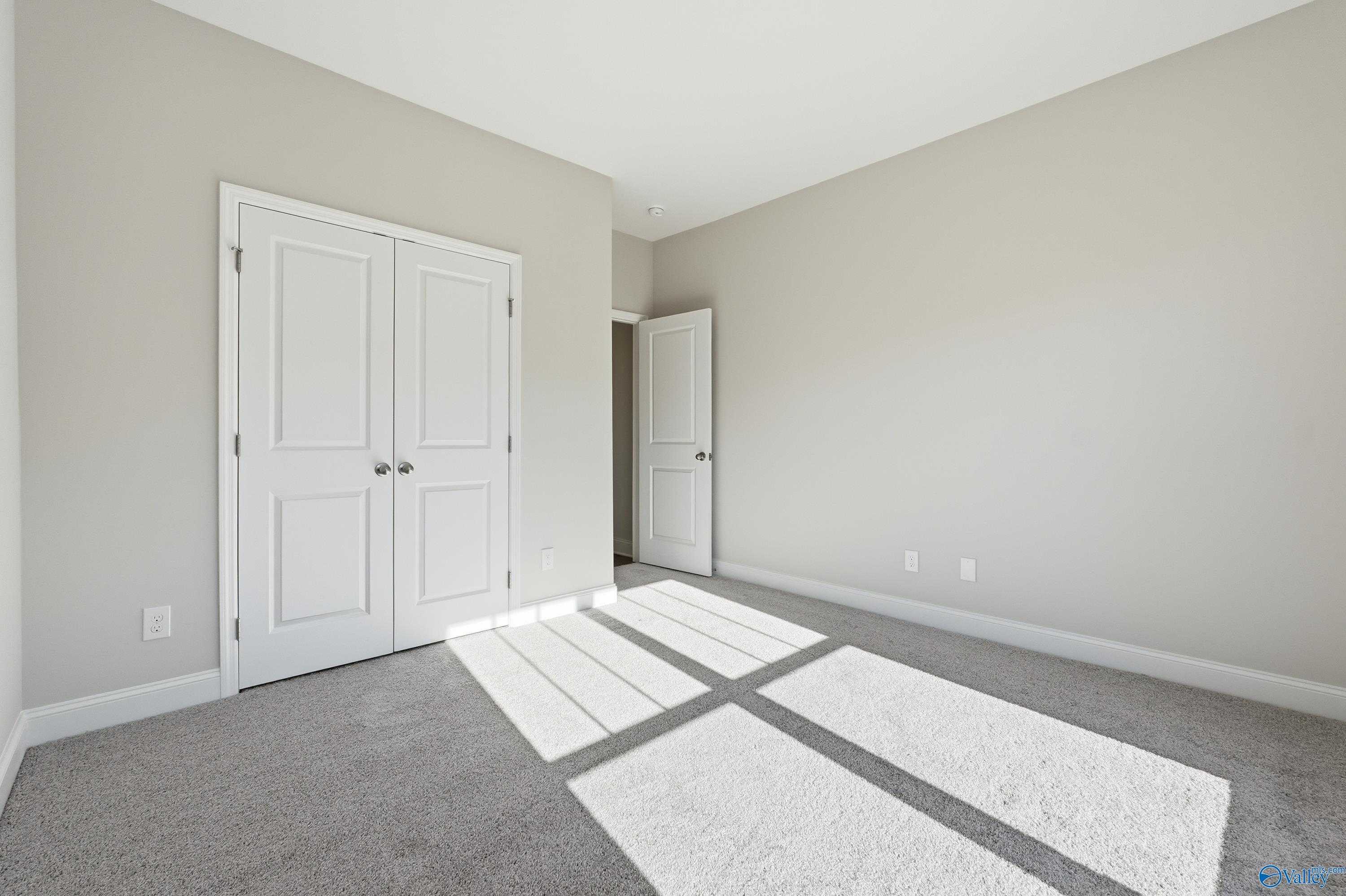 Bright bedroom featuring neutral walls, white double closet doors, carpet floor, and natural sunlight in Davidson Homes The Everett, Harvest AL