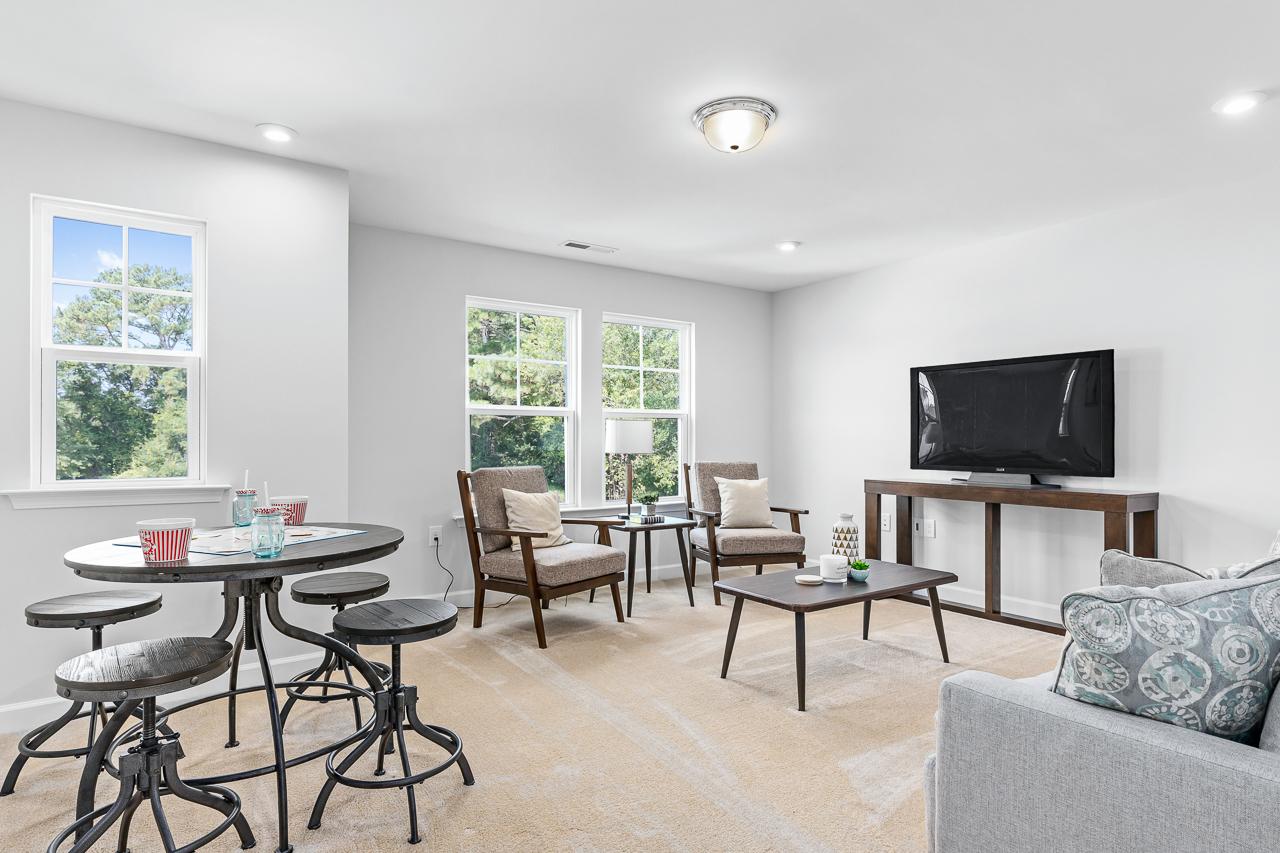 Spacious living room at Stagecoach Corner in Mebane NC with round pedestal table, mounted TV, gray sofa, armchairs, and large windows