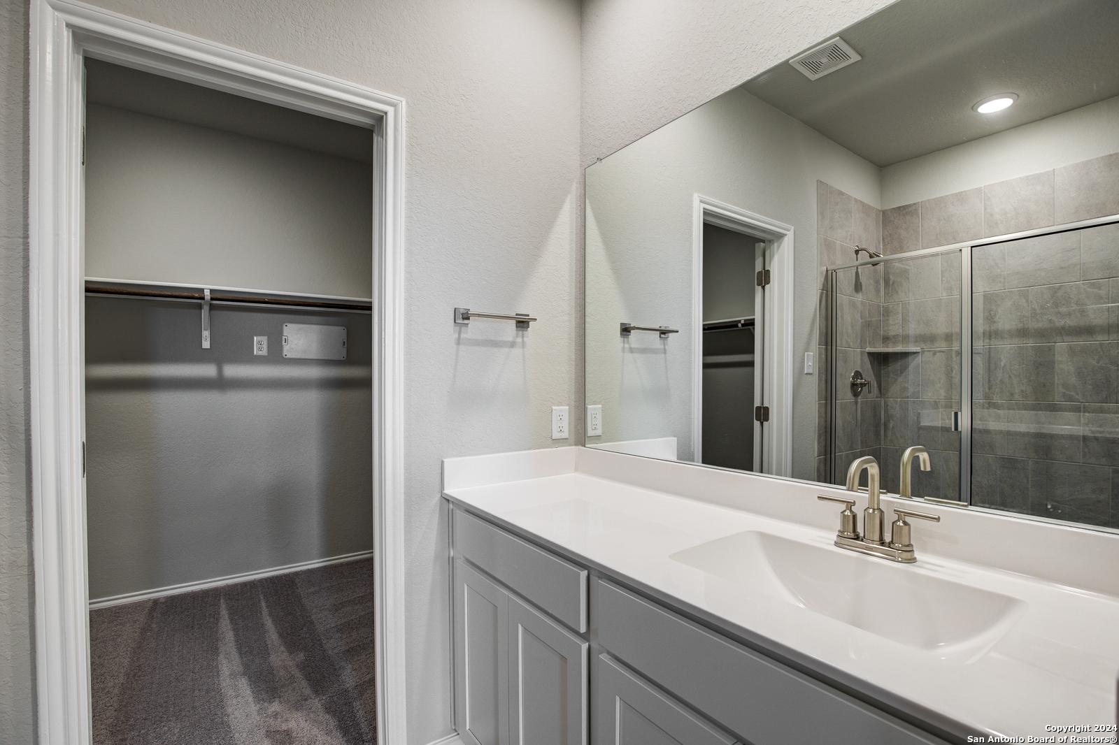 Modern master bathroom with double vanity, large mirror, walk-in closet, and frameless glass shower in Davidson Homes Blanco C, San Antonio