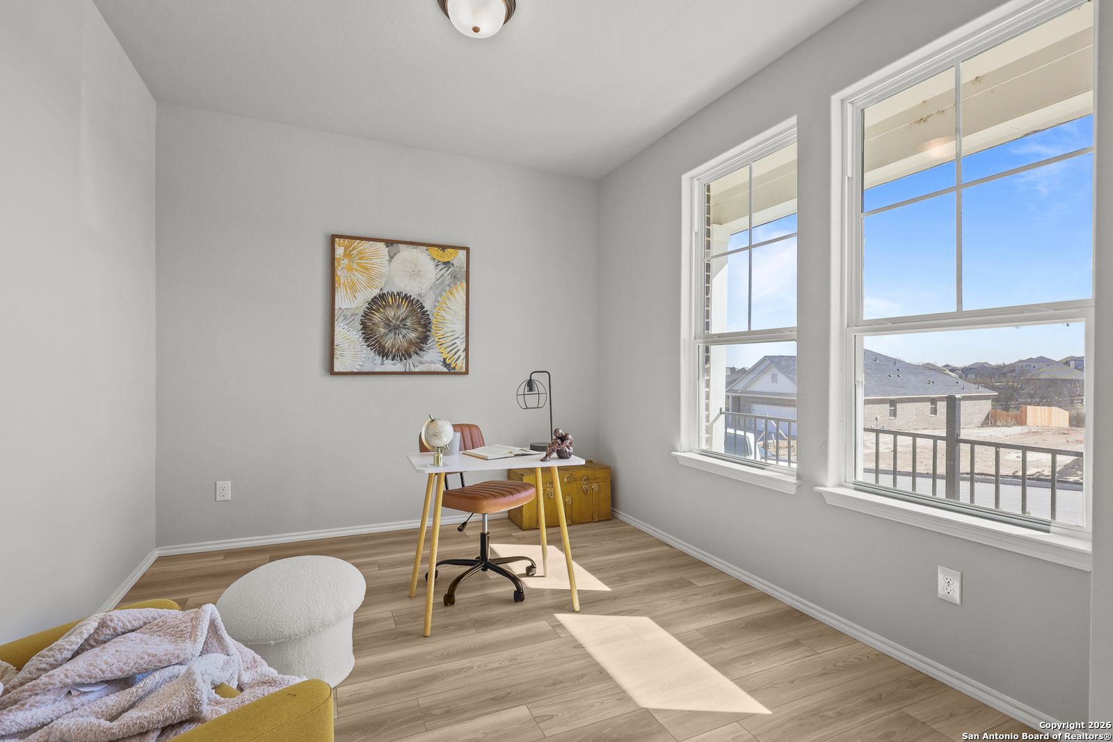 Bright home office with large windows, modern desk, abstract floral art, and hardwood floors in Davidson Homes The Murray K, San Antonio