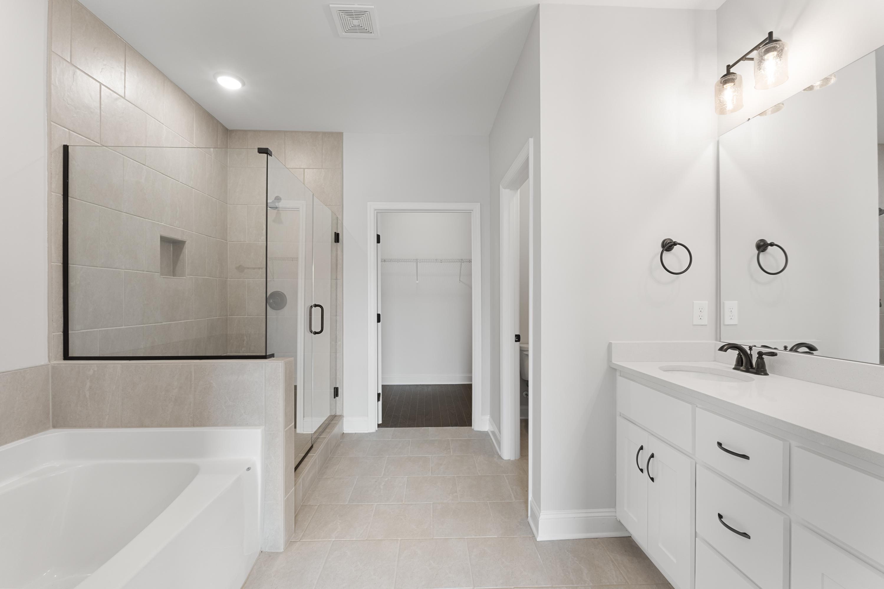 Spacious master bathroom in The Copeland featuring frameless glass shower, soaking tub, and double white vanity