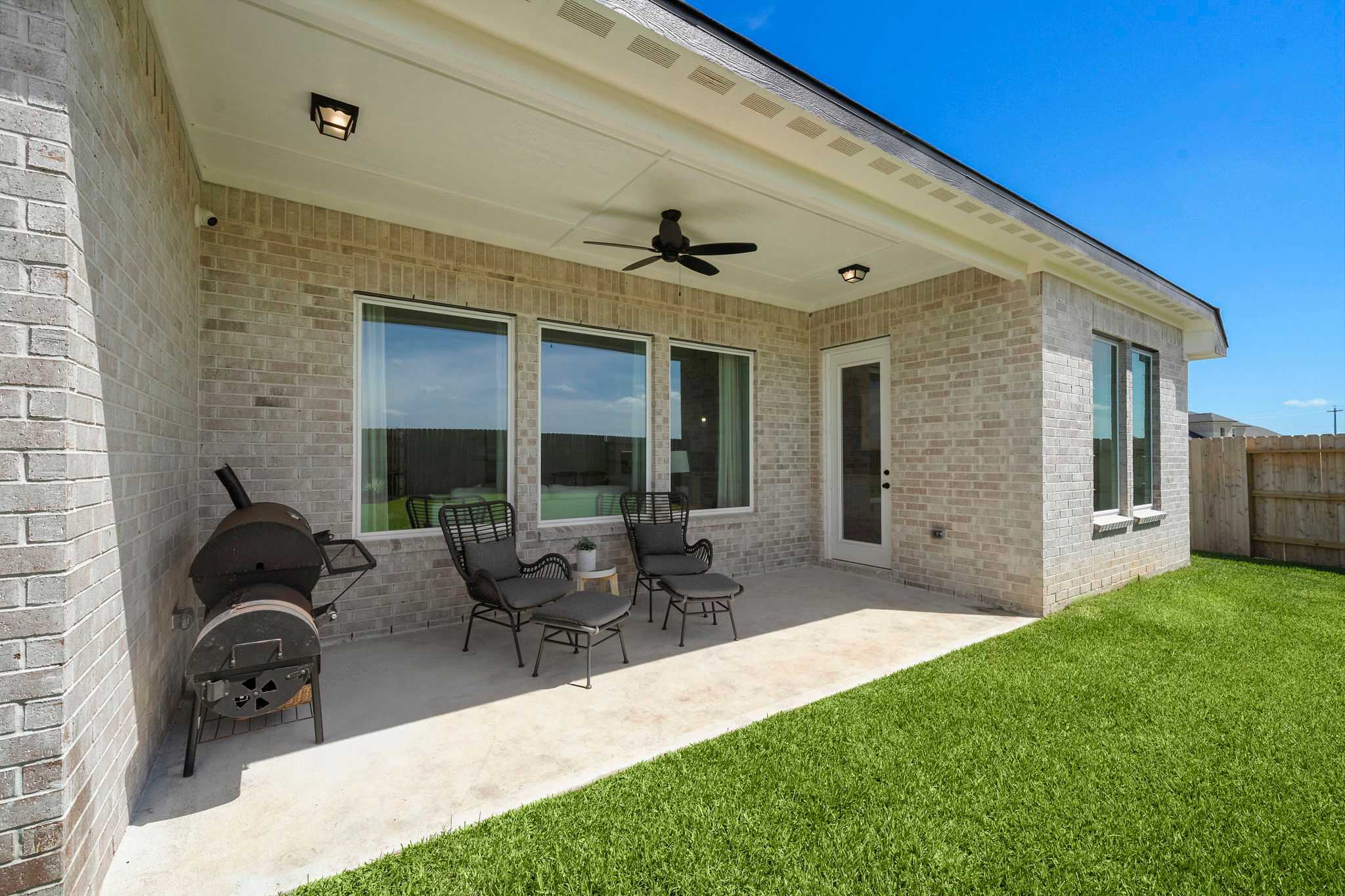 Covered patio with ceiling fan, grill, and lounge chairs at Lago Mar in Texas City, Texas by Davidson Homes on lush green lawn