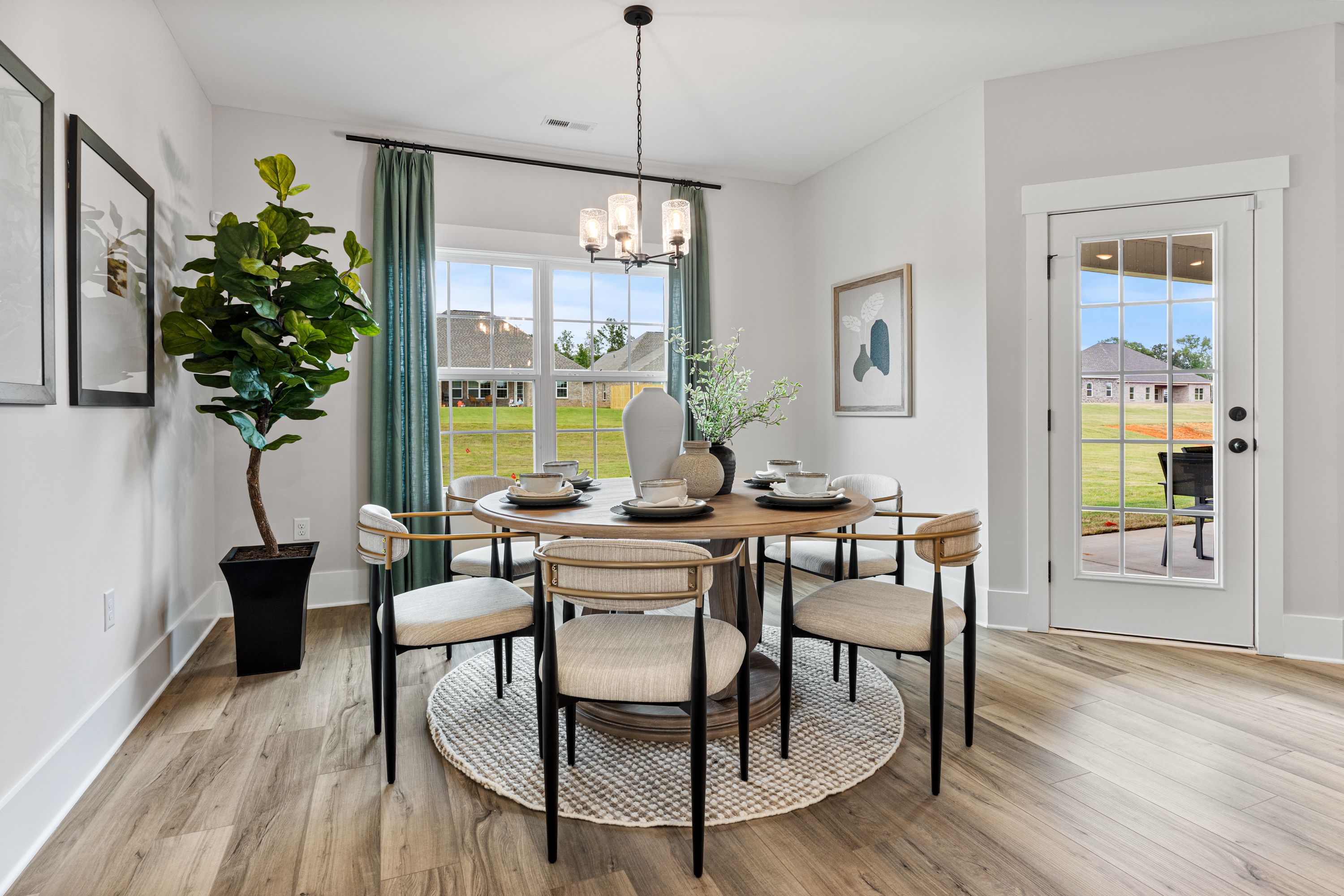 Spacious dining room at River Road Estates in Decatur Alabama with round wooden table, upholstered chairs, chandelier, and garden view through large windows