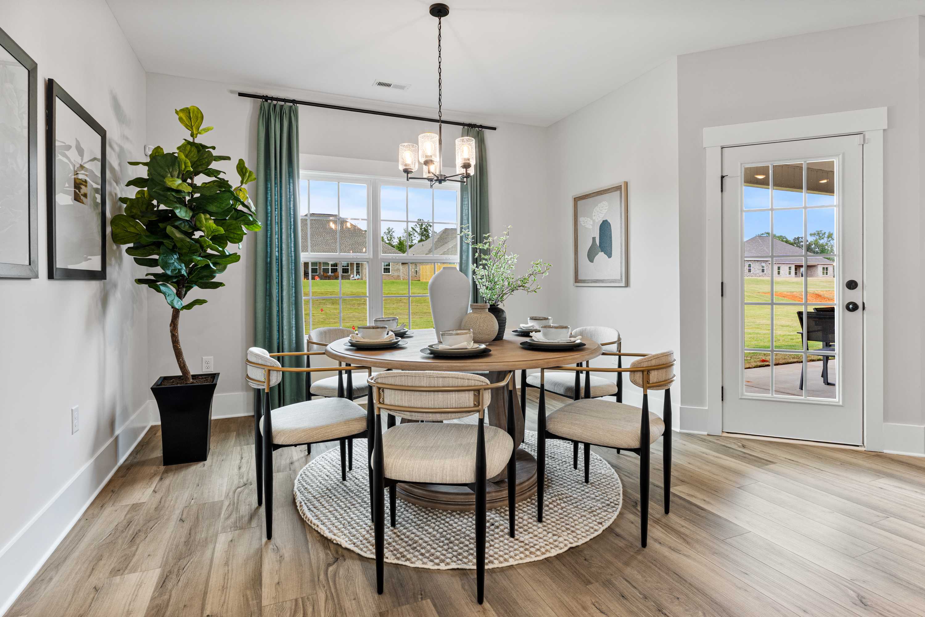 Spacious dining room at River Road Estates in Decatur Alabama with round wooden table, upholstered chairs, chandelier, and garden view through large windows