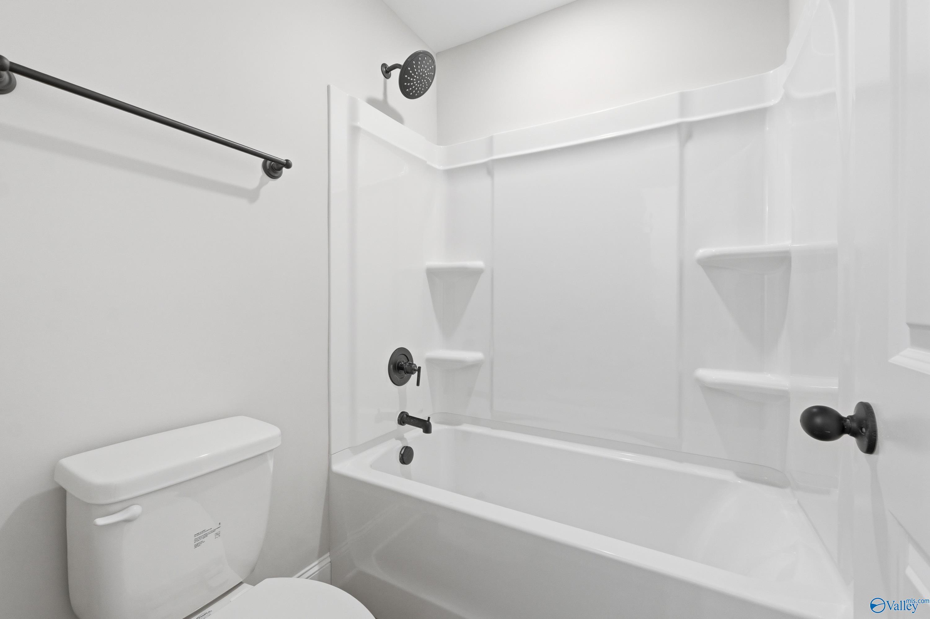 Bright white bathroom with bathtub, glass shower enclosure, built-in shelves, and black fixtures in Davidson Homes The Chelsea D, Cullman, Alabama