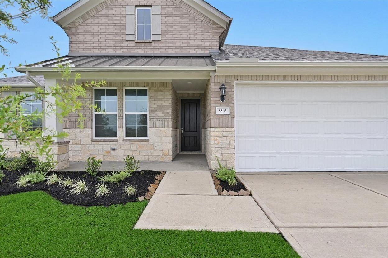 Beige brick single-story home with 3-car garage, covered front porch, stone accents, and lush landscaping in Lago Mar, Texas City