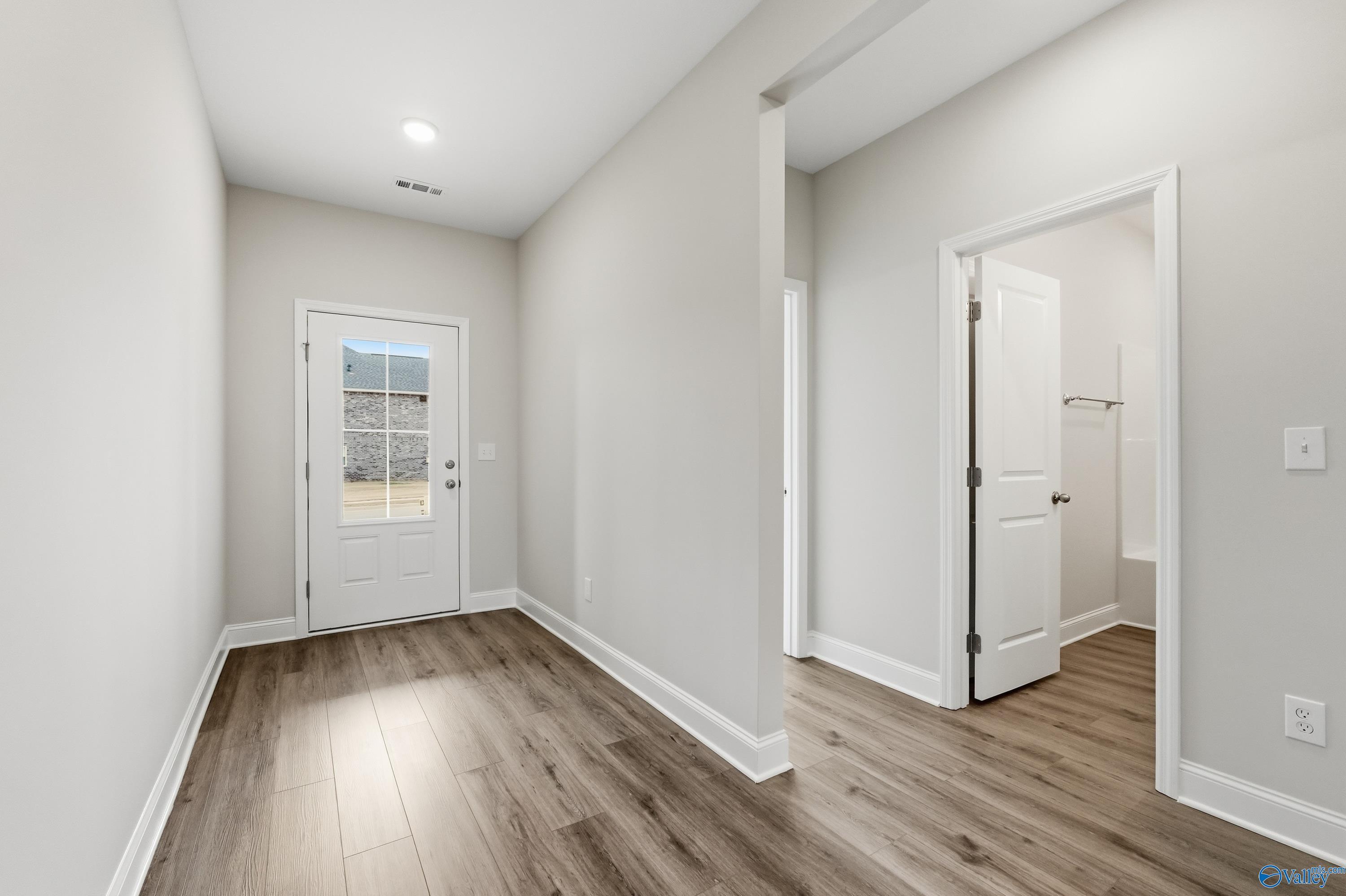 Bright entry hallway with light gray walls, laminate wood floors, and open doors in Davidson Homes The Daphne C, Toney, Alabama