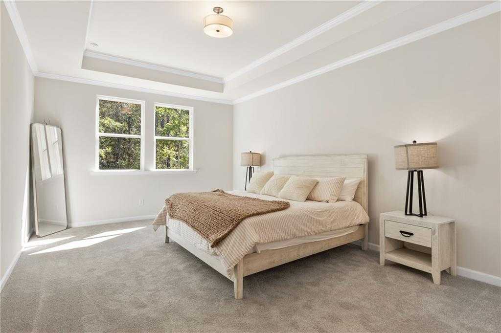 Elegant master bedroom with king bed, tray ceiling, large windows, and neutral tones in Davidson Homes The Daphne B, Loganville, GA