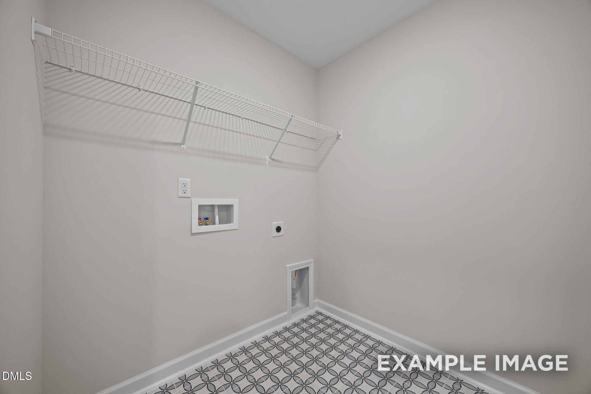 Spacious laundry room with white wire shelving, washer hookups, dryer vent, and gray patterned tile floor in Davidson Homes The Avery, Knightdale, NC