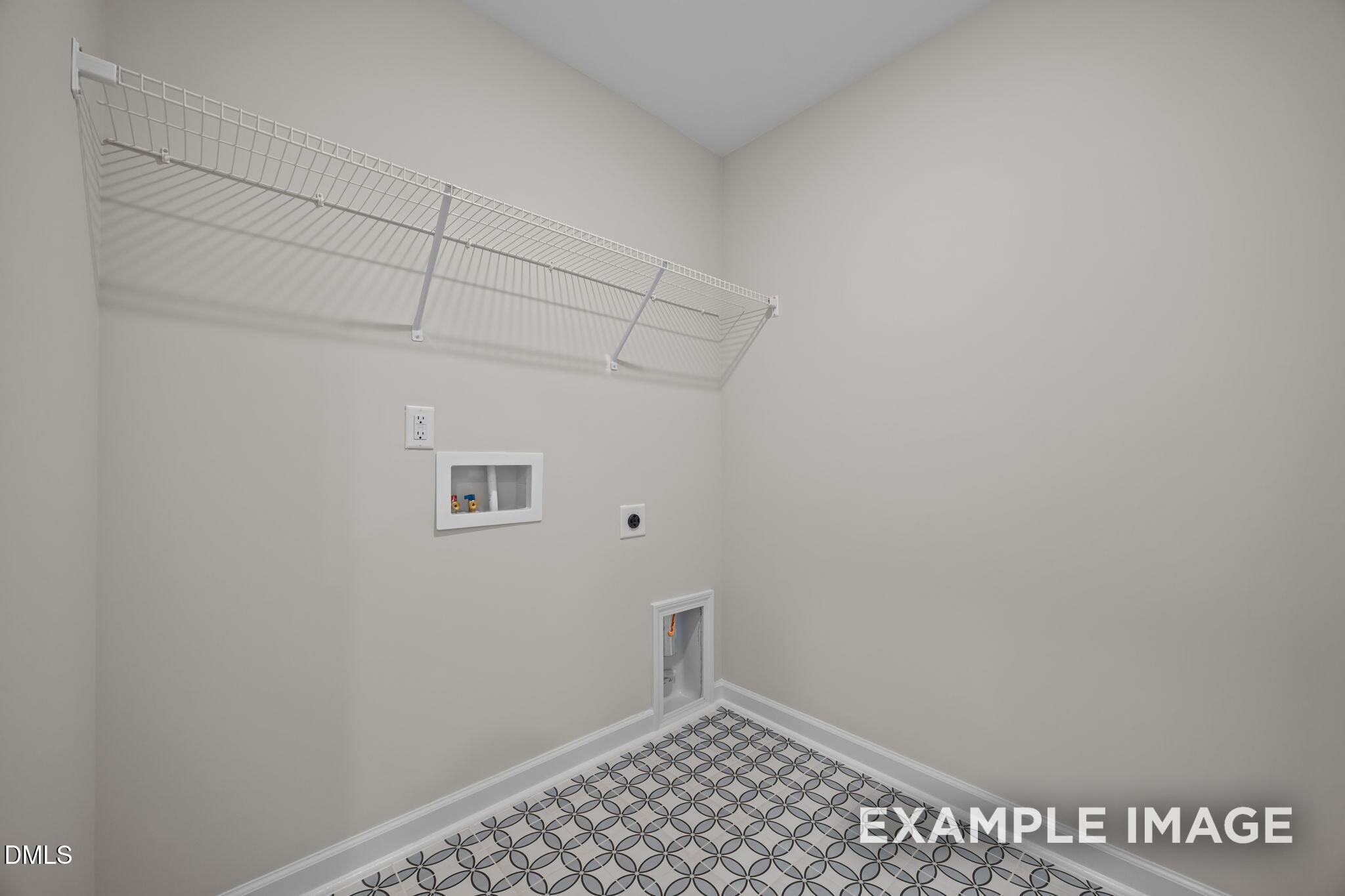 Spacious laundry room with white wire shelving, washer hookups, dryer vent, and gray patterned tile floor in Davidson Homes The Avery, Knightdale, NC