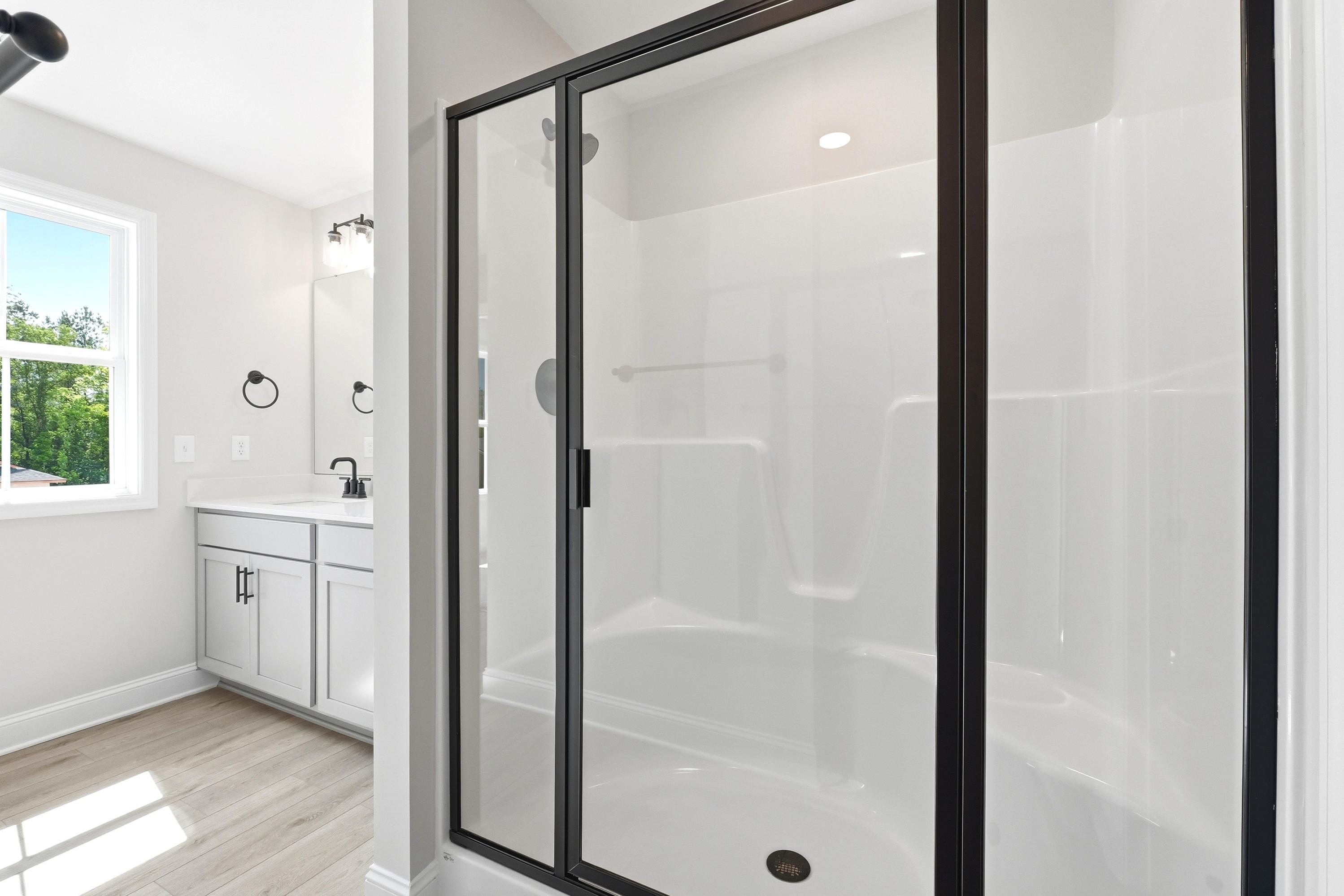 Modern master bathroom in The Russell A featuring a walk-in shower with black frame and white vanity with matte black trim.