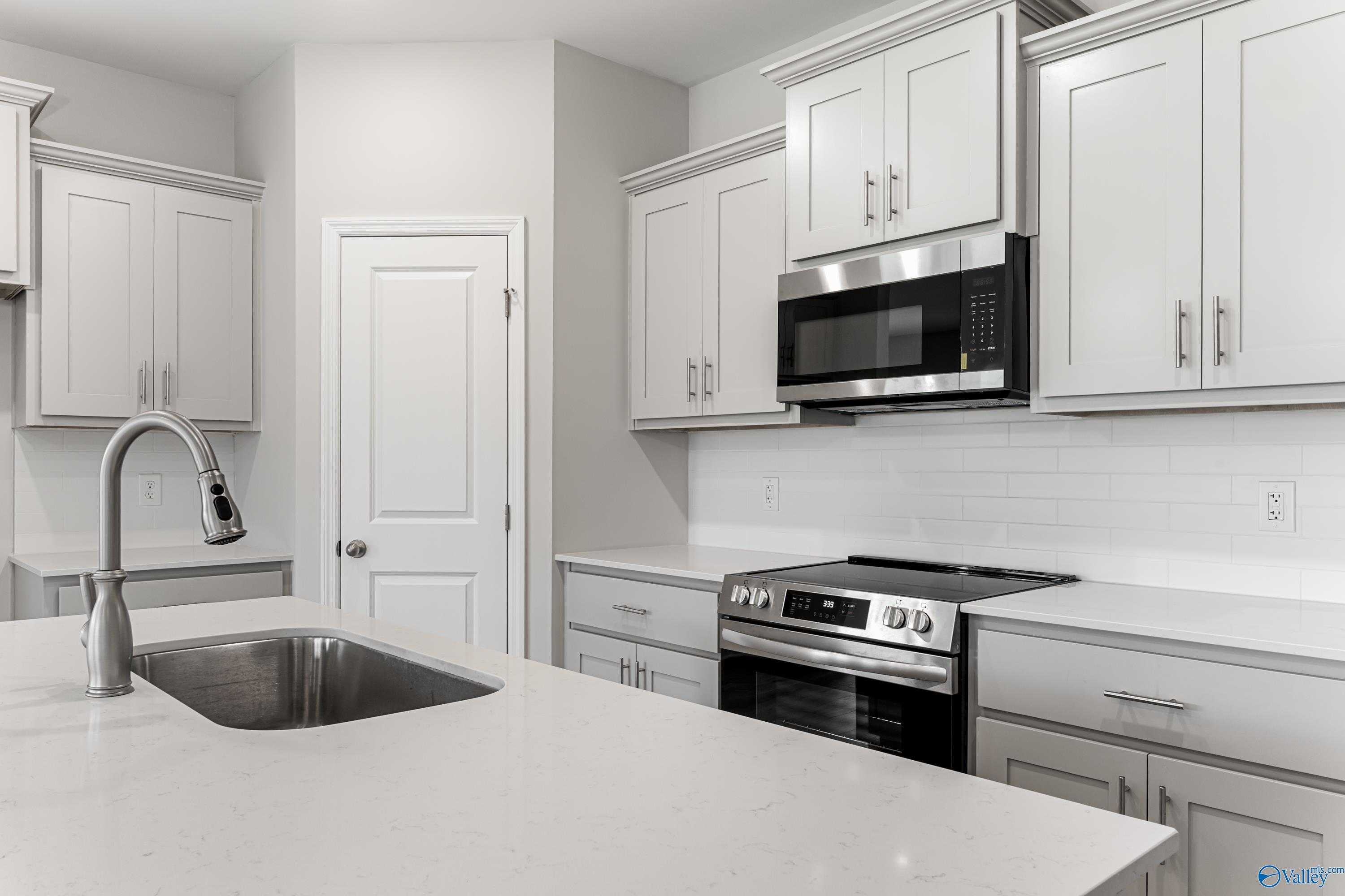 Modern white kitchen featuring quartz countertops, stainless steel appliances, subway tile backsplash in The Daphne C, Athens, Alabama