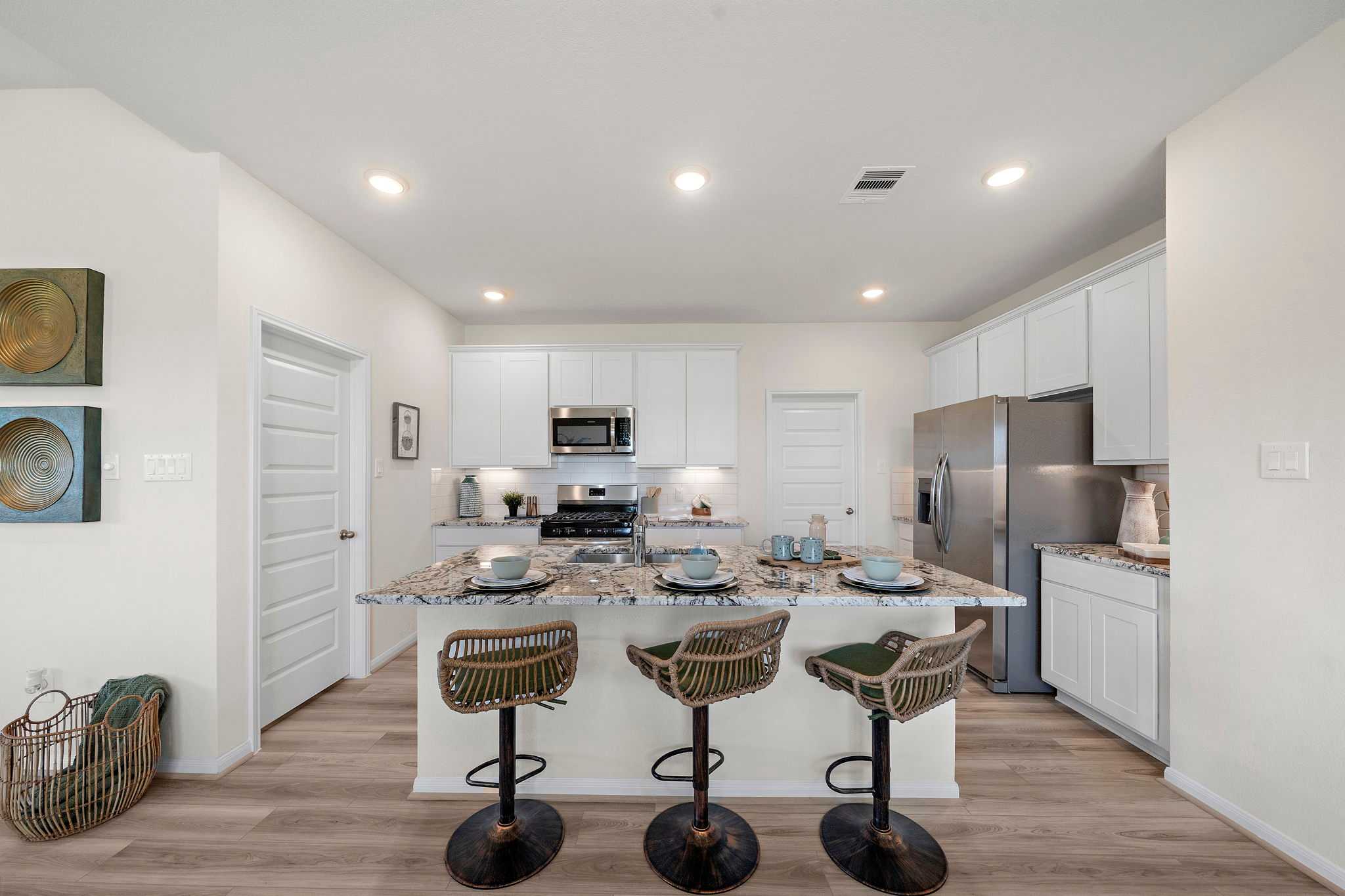 Spacious white kitchen with granite island, rattan bar stools, stainless appliances, and hardwood floors at River Ranch Meadows in Dayton TX