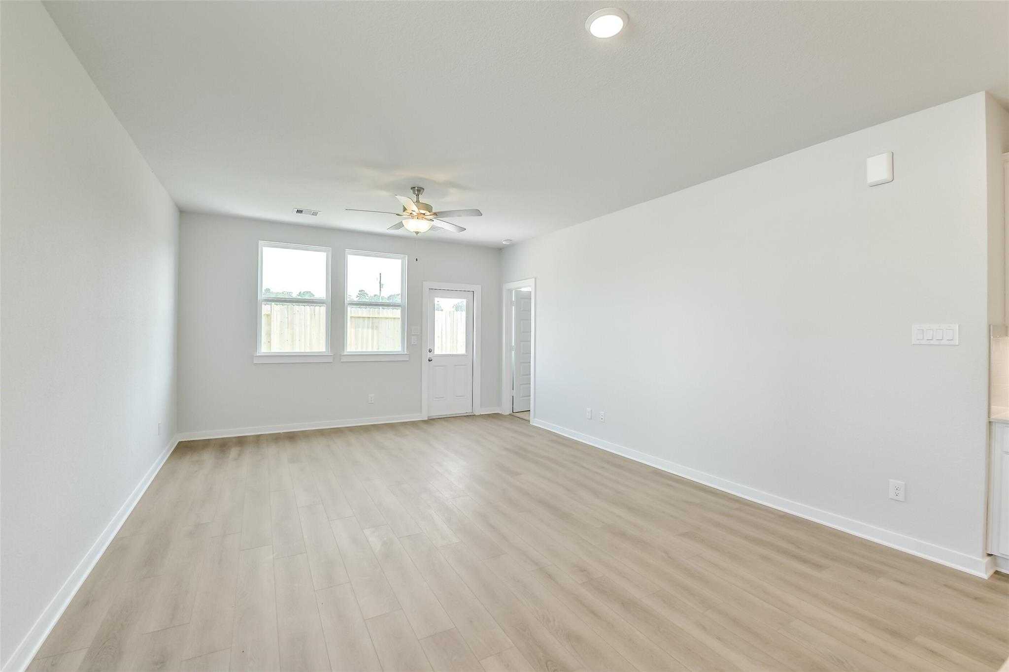 Spacious open living room with hardwood floors, ceiling fan, and large windows in Davidson Homes The Colorado F, Cleveland Texas