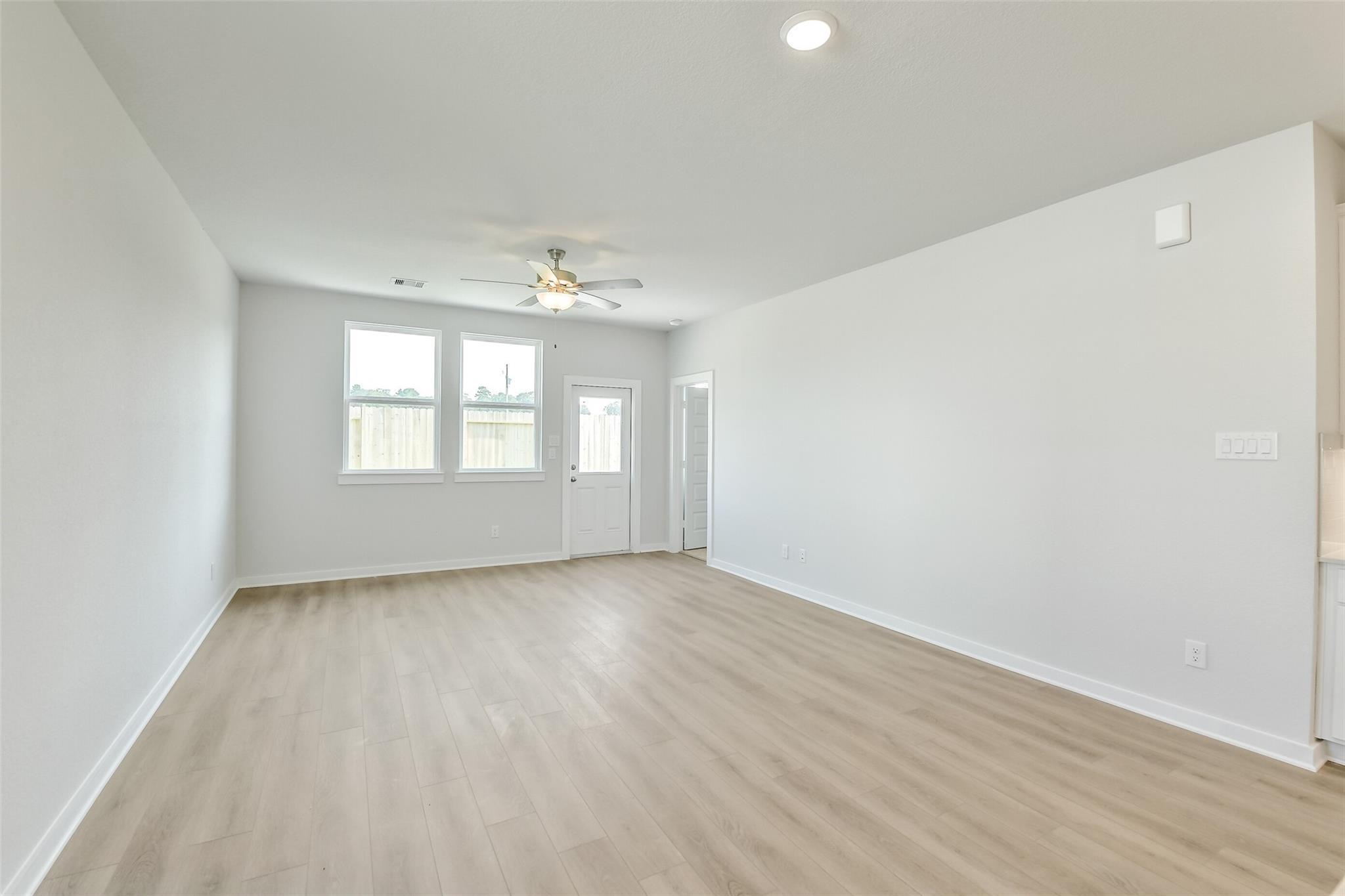 Bright open living room with ceiling fan, large windows, and light wood floors in Davidson Homes Colorado F, Cleveland TX