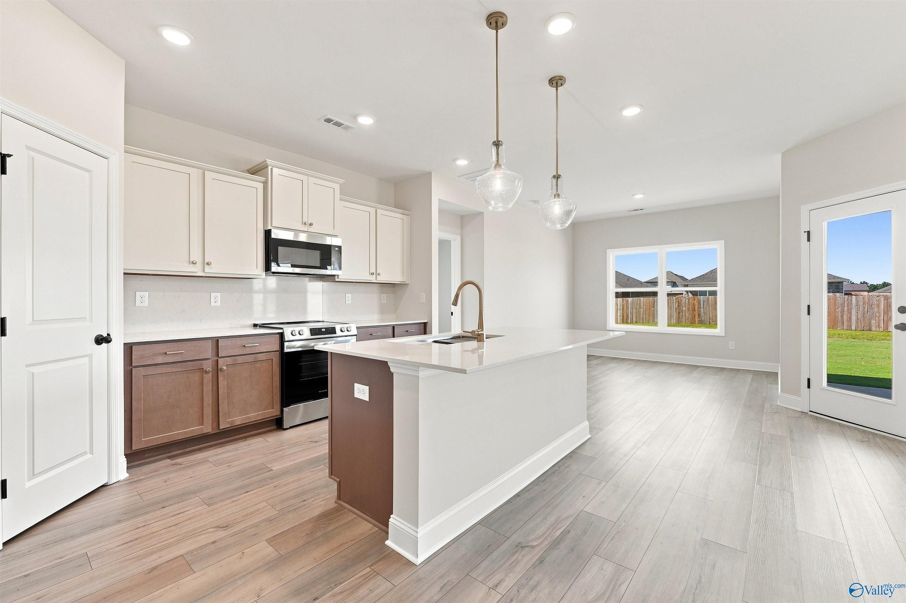 Open-concept kitchen with island, white cabinets, and luxury vinyl flooring in Davidson Homes The Everett B plan, Toney, Alabama