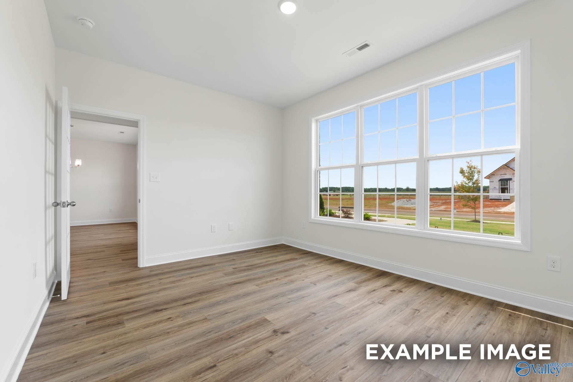 Bright empty room with hardwood floors and large windows overlooking green fields in Davidson Homes The Oxford, Huntsville, Alabama