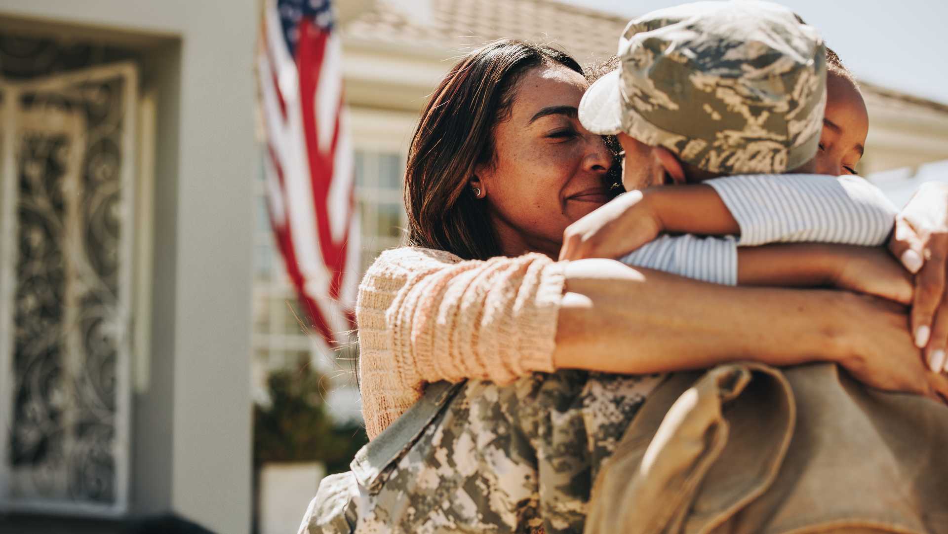 Heartwarming military family embrace outside new Raleigh home, American flag waving for hometown heroes promotion