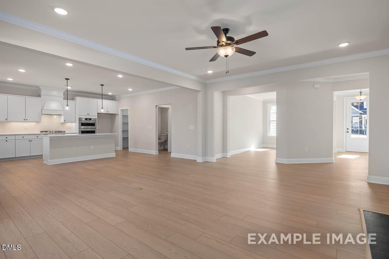 Open-concept kitchen-living area with white cabinets, light oak floors, ceiling fan in Davidson Homes The Crawford D, Angier, NC