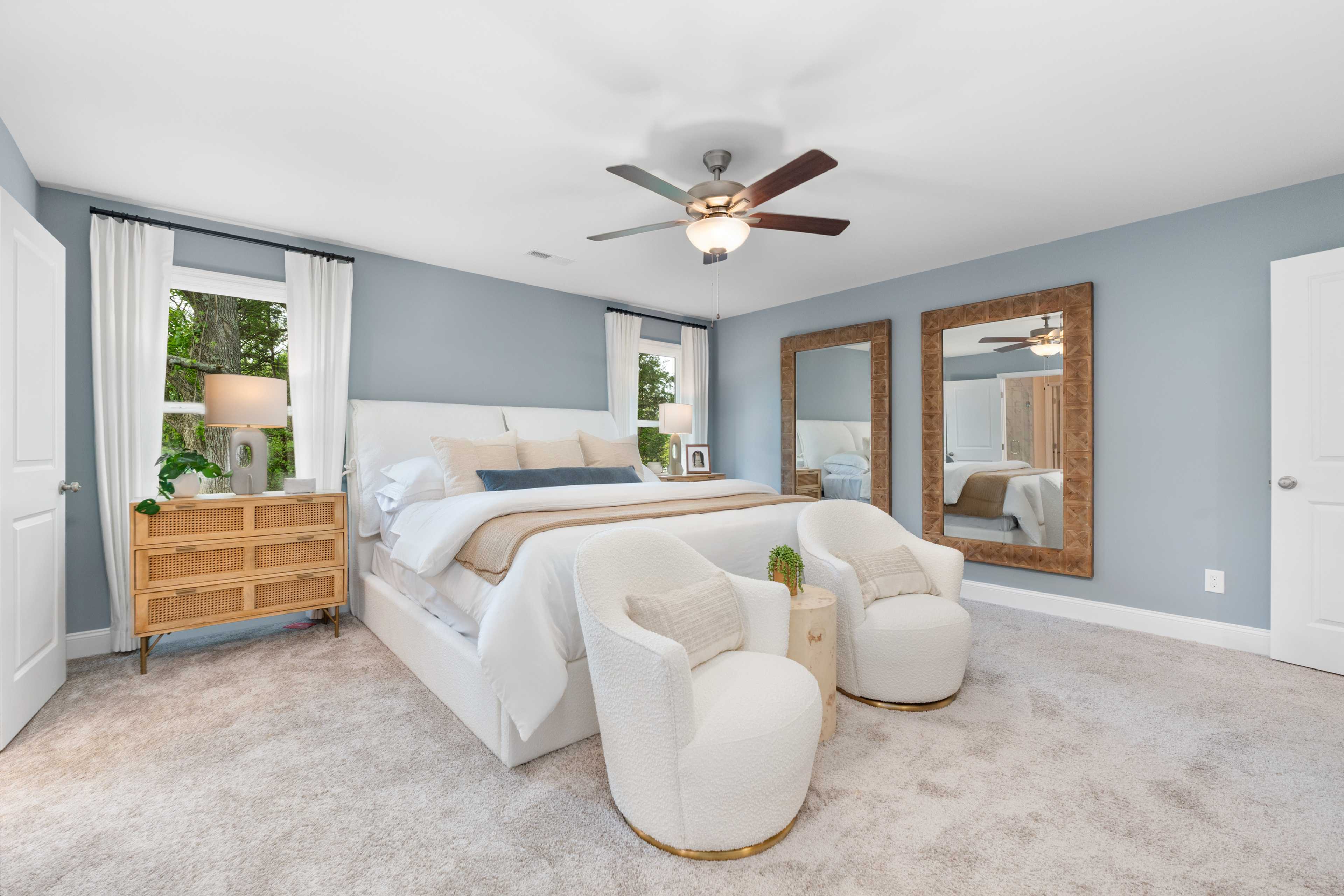 Spacious primary bedroom in Pavilion Huntsville Alabama with light blue walls, king bed, wooden mirrors, and accent chairs
