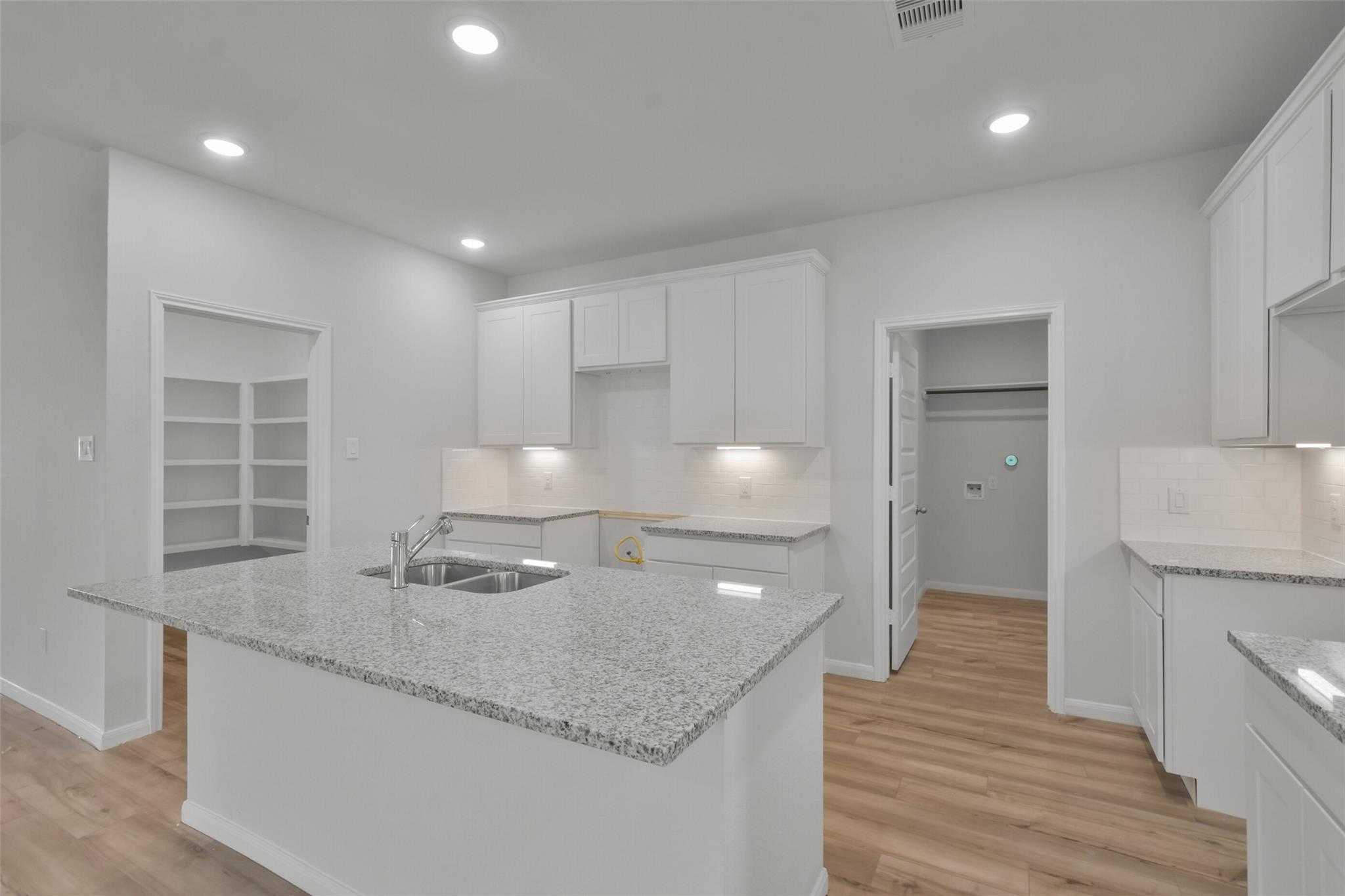 Modern white kitchen with granite island sink and open shelving in Davidson Homes The Tierra A, Dayton, Texas