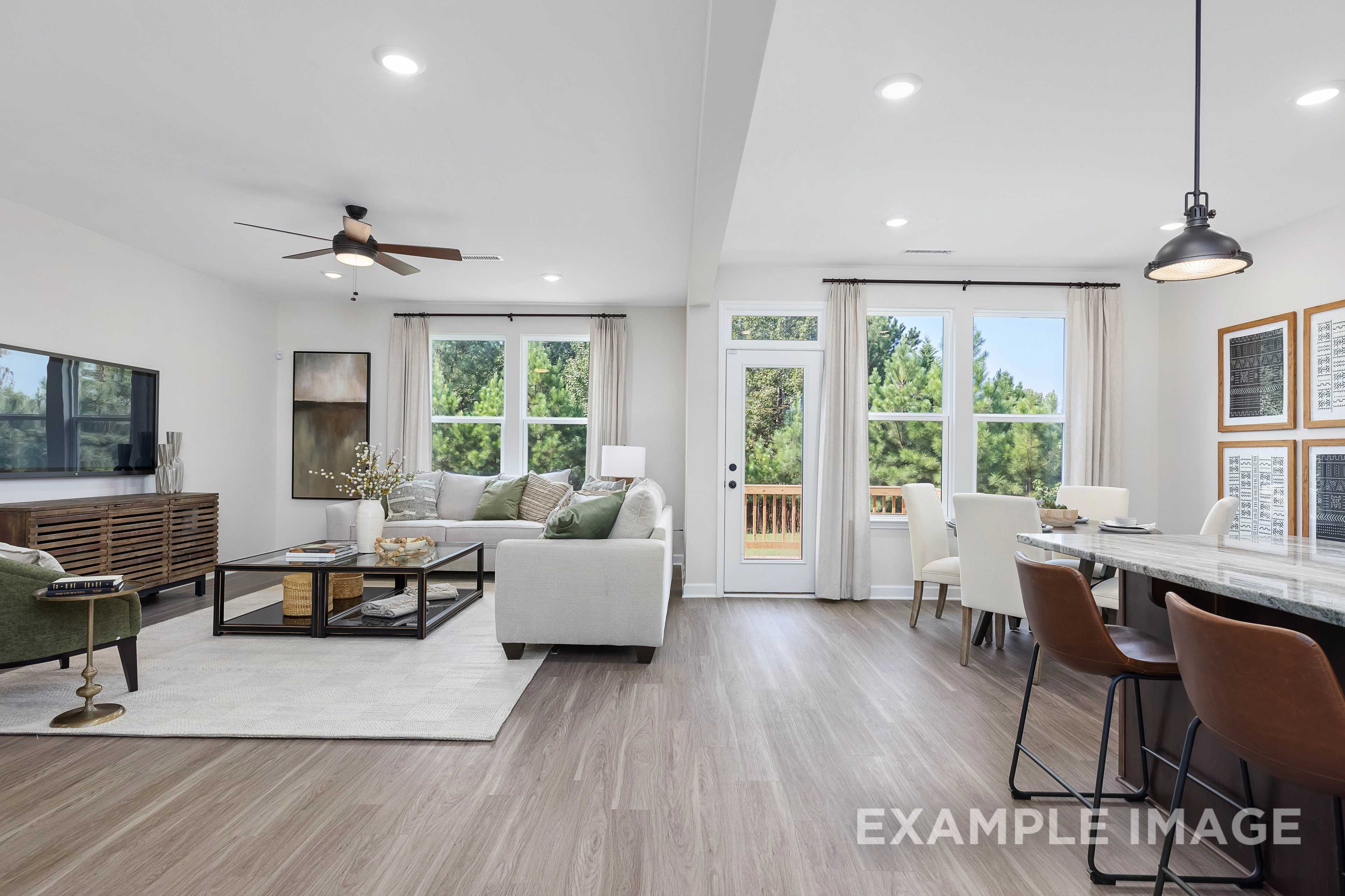 Spacious open-concept living room in The Willow B with white sofa, TV console, French doors to deck, dining table, kitchen island, and hardwood floors
