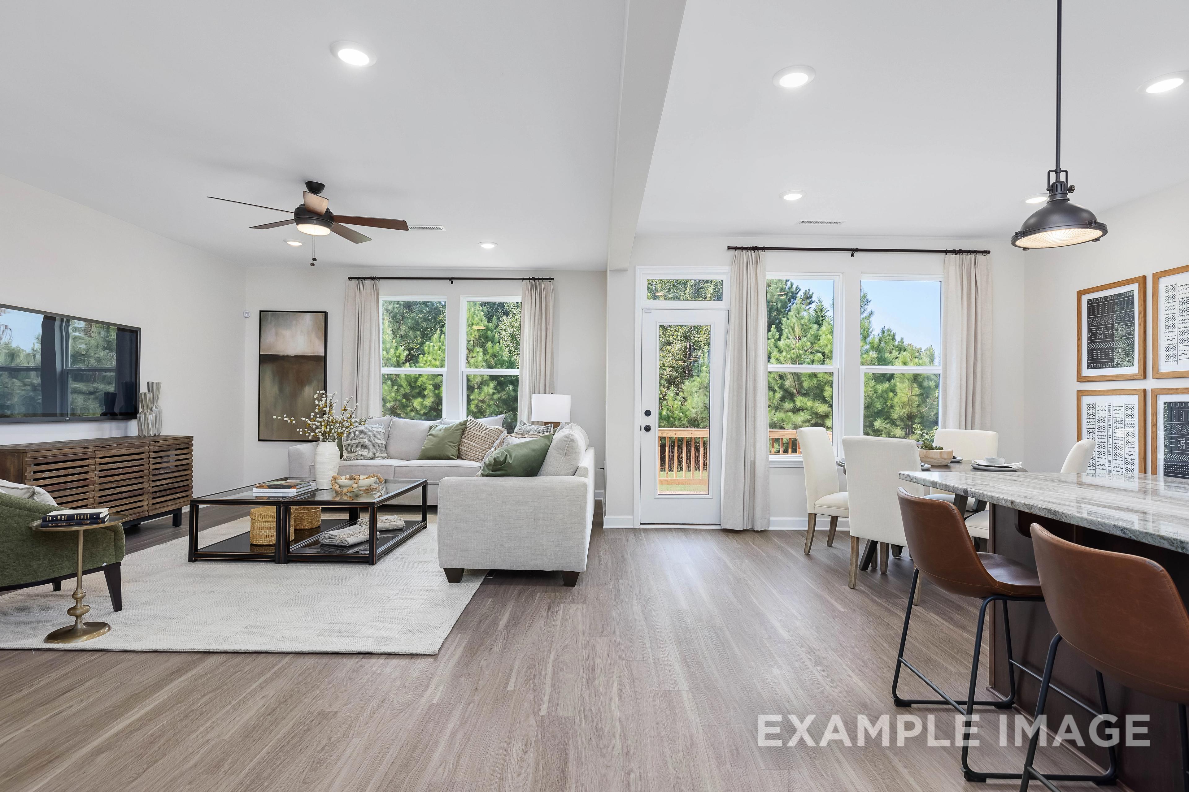 Spacious open-concept living room in The Willow B with white sofa, TV console, French doors to deck, dining table, kitchen island, and hardwood floors