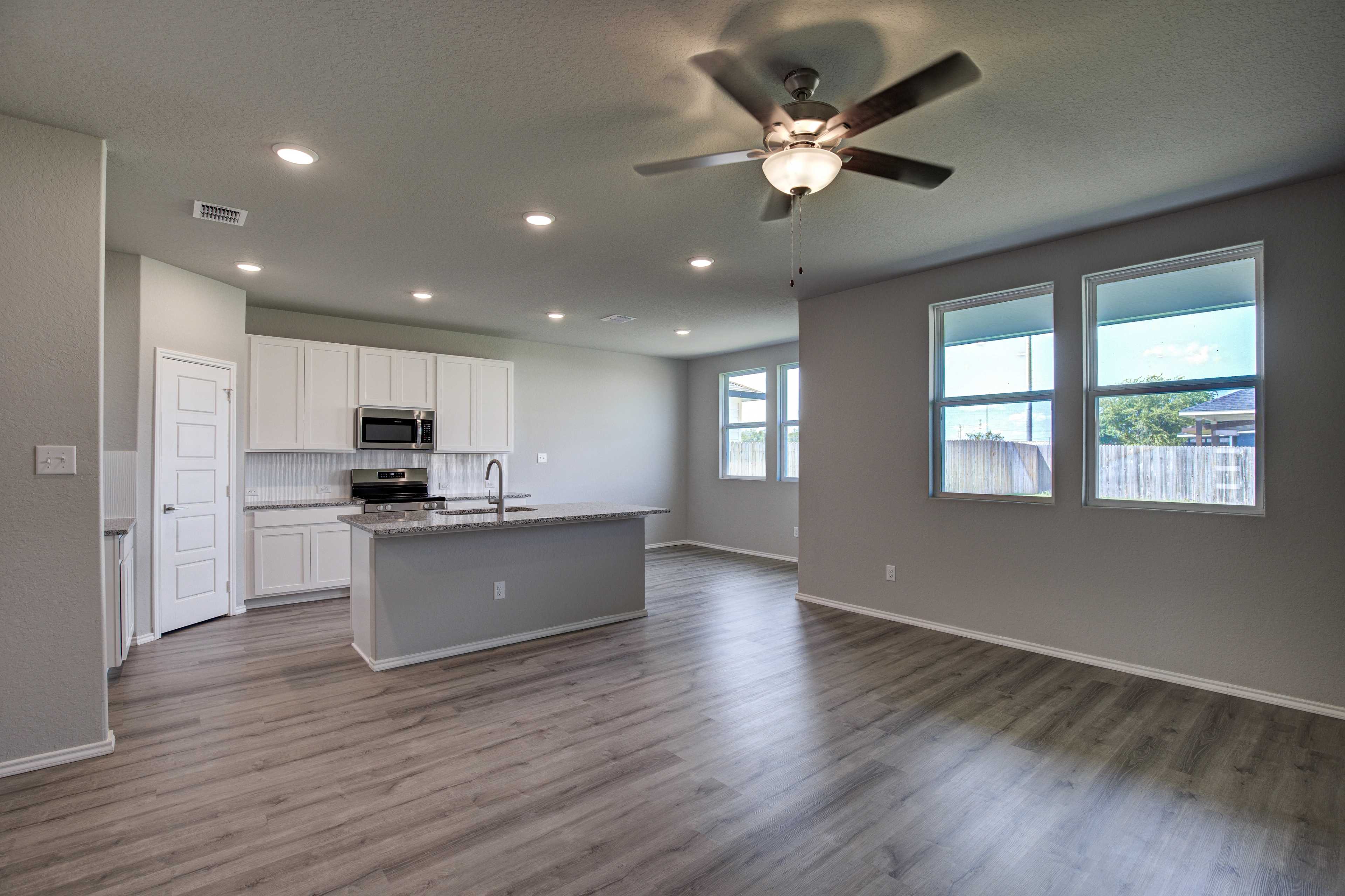 Spacious open-concept kitchen in The Asheville with white cabinets, large island sink, stainless appliances, ceiling fans, and light wood floors