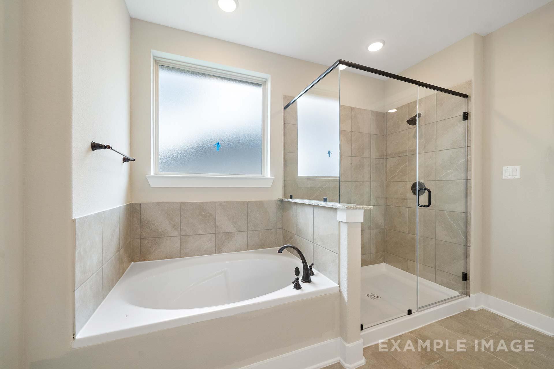 Spacious master bathroom in The Elizabeth A featuring frameless glass shower, deep soaking tub, and neutral tile accents