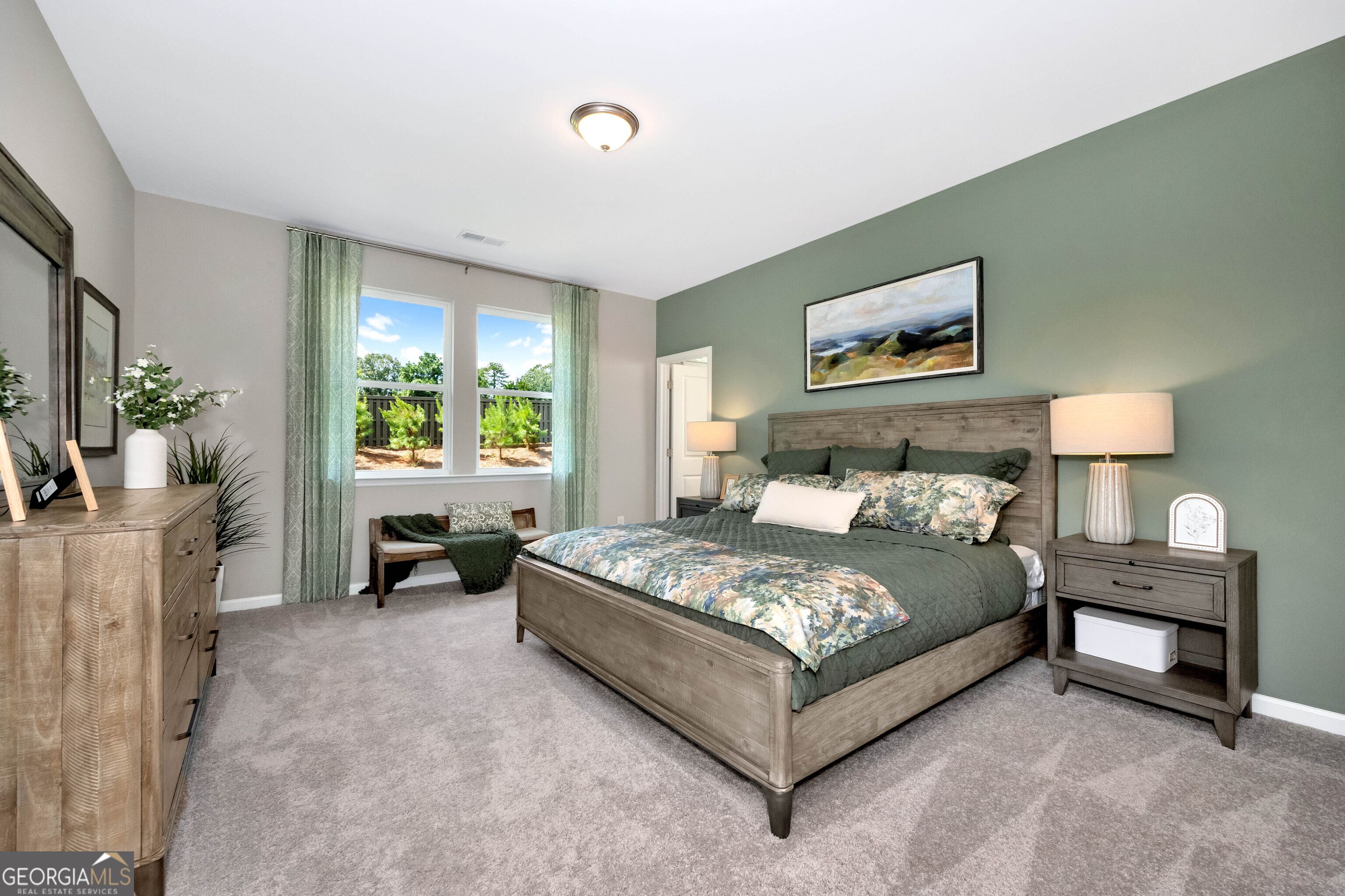 Elegant sage green master bedroom with wooden king bed, floral bedding, and large window in The Stella by Evermore Homes, Perry, GA