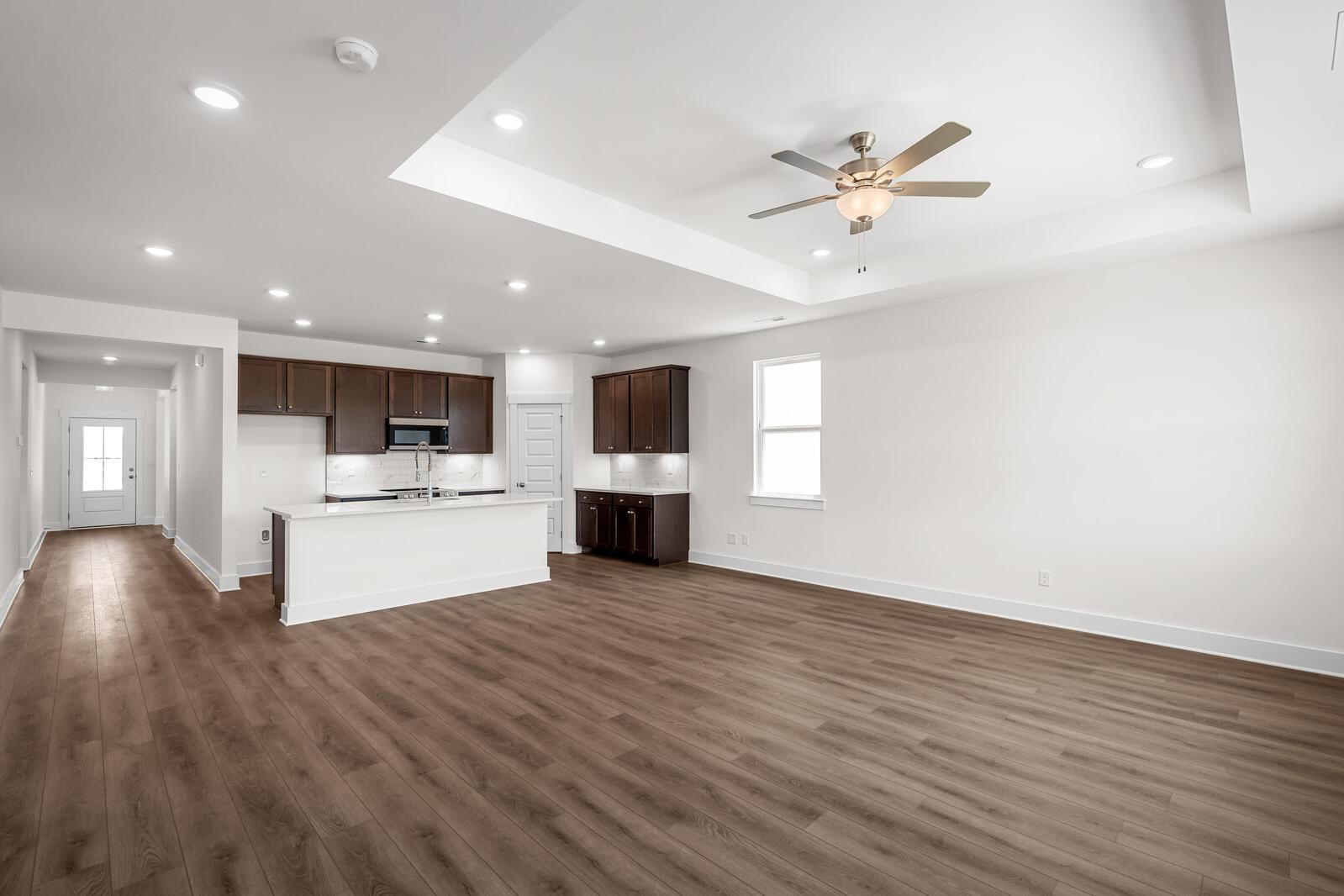 Open-concept kitchen and living area in The Cottonwood by Davidson Homes featuring dark cabinetry and tray ceilings.