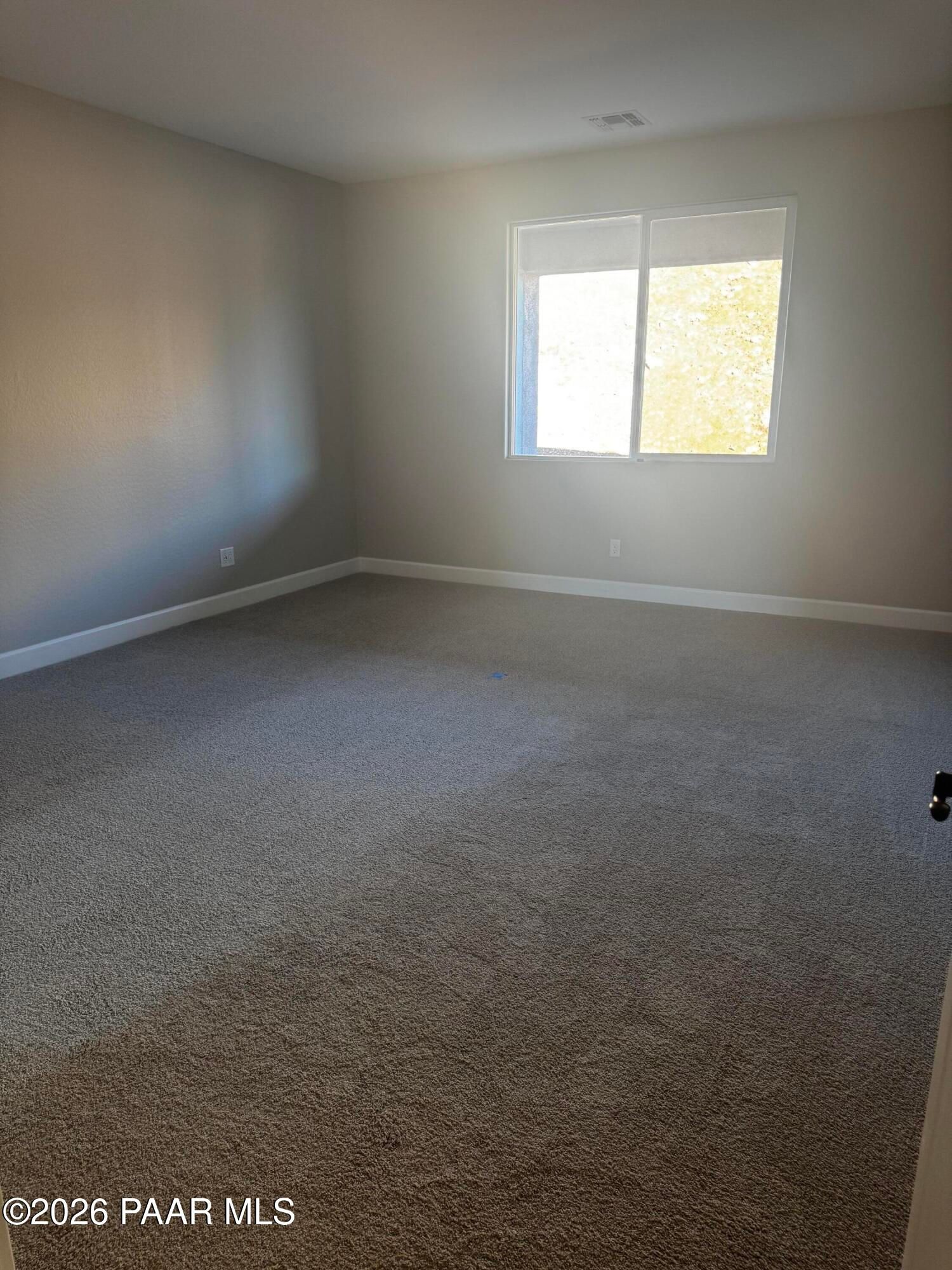 Bright empty bedroom with large sunny window, neutral walls, and beige carpet in Evermore Homes The Monarch B, Prescott Valley