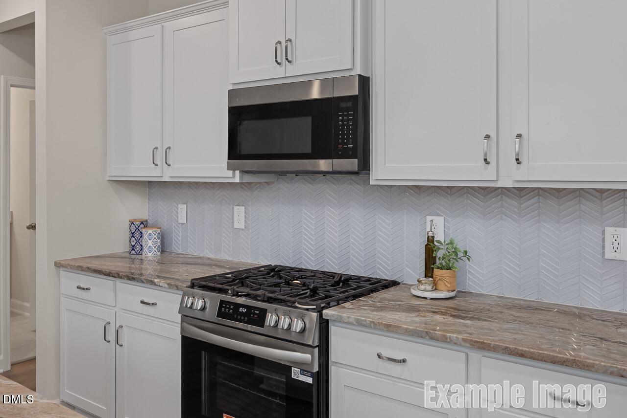 Modern kitchen featuring white shaker cabinets, stainless steel range and microwave, herringbone tile backsplash in Davidson Homes The Carter C, Lillington, NC