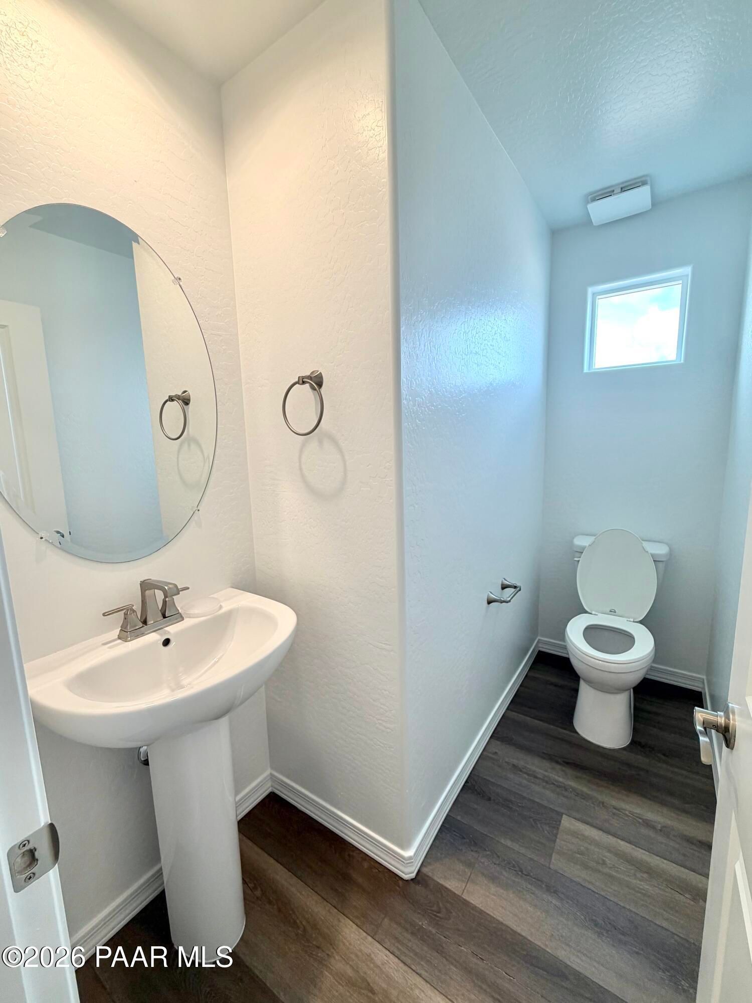 Half bath with pedestal sink, oval mirror, and wood-look flooring in The Raleigh A floor plan, South Ranch, Prescott, AZ.