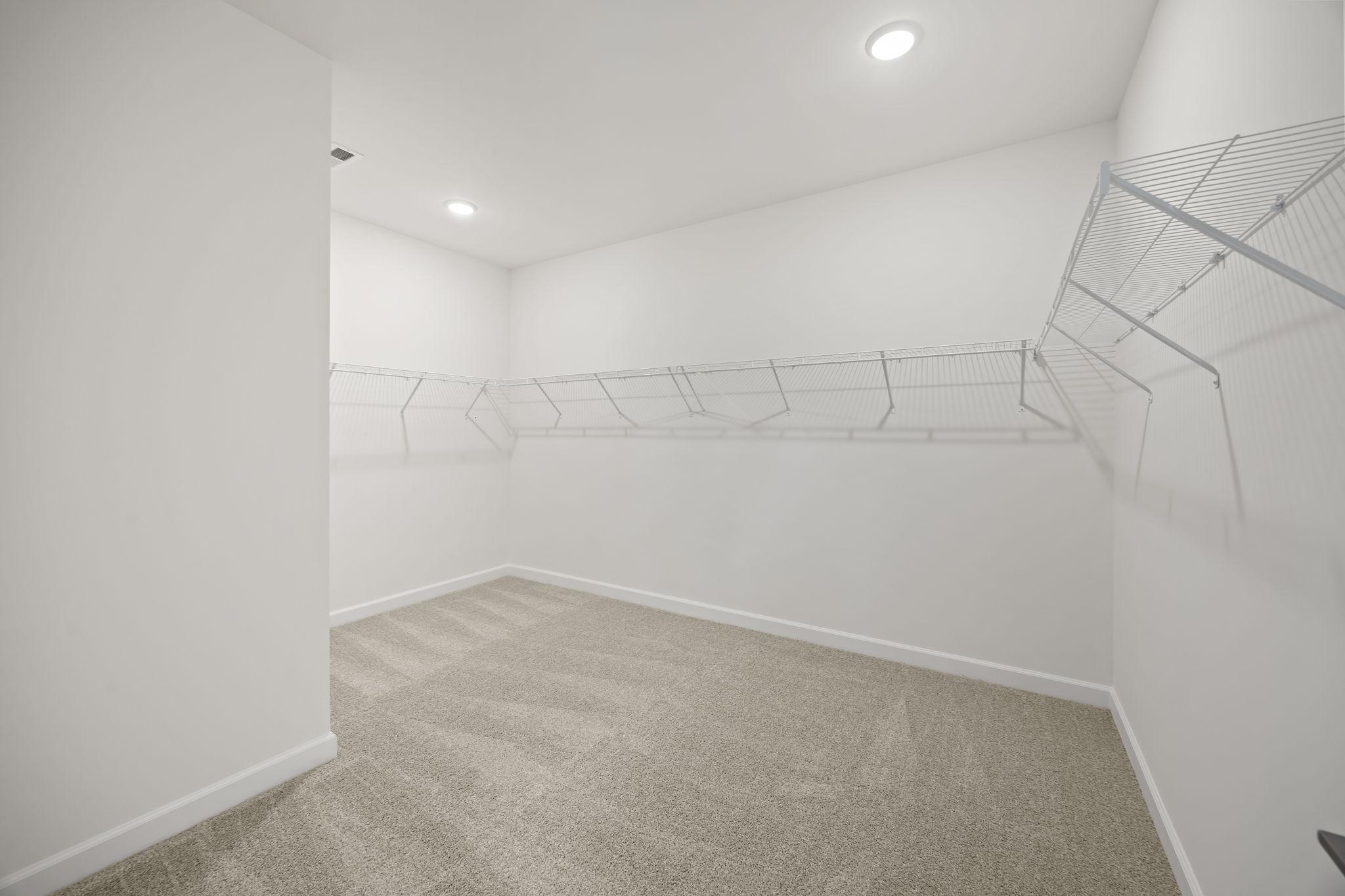 Spacious walk-in closet with white wire shelving and plush carpeting at Rockport in Wake Forest, NC by Davidson Homes.