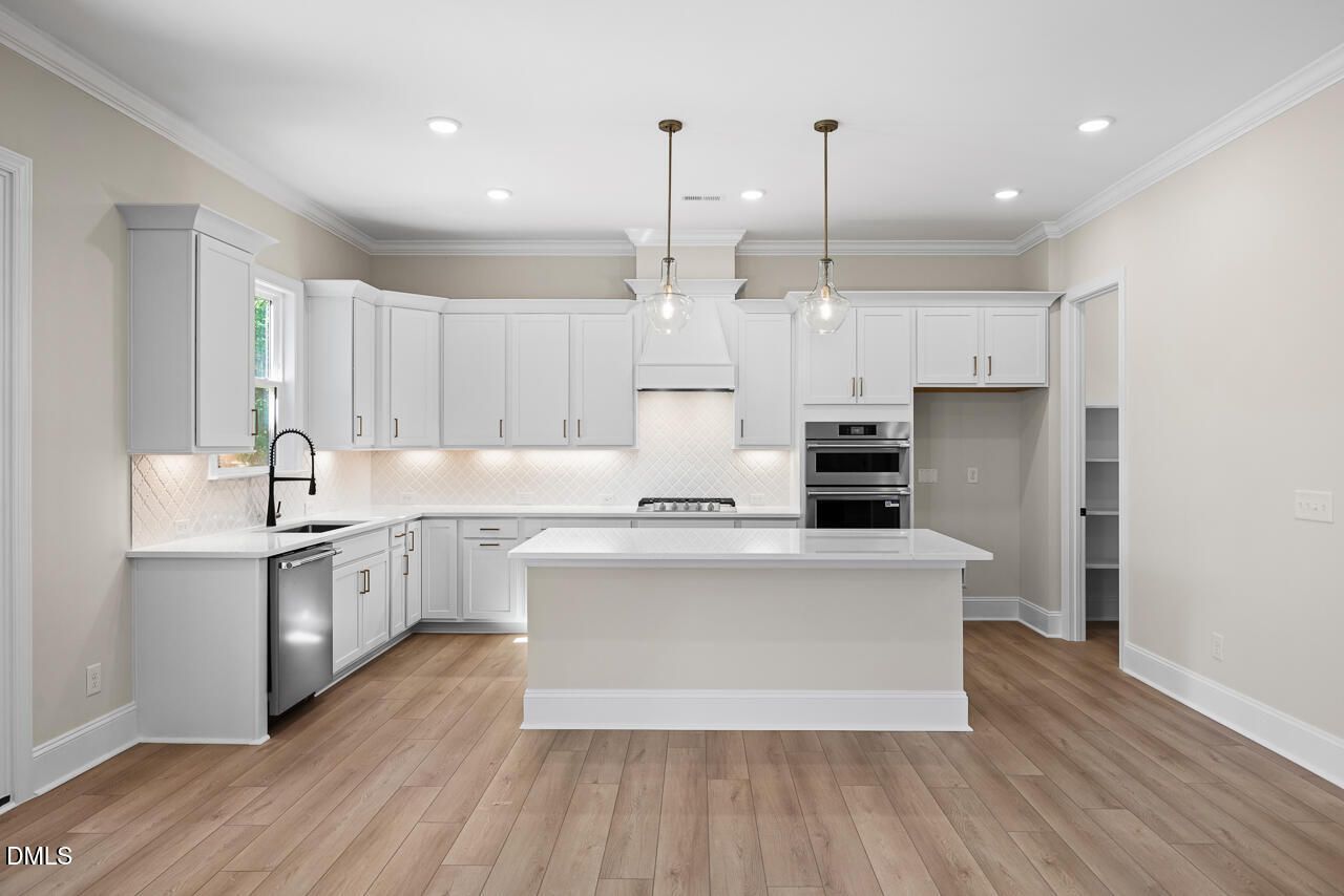 White kitchen with large center island, pendant lights, stainless appliances, and hardwood floors in Davidson Homes Crawford D plan