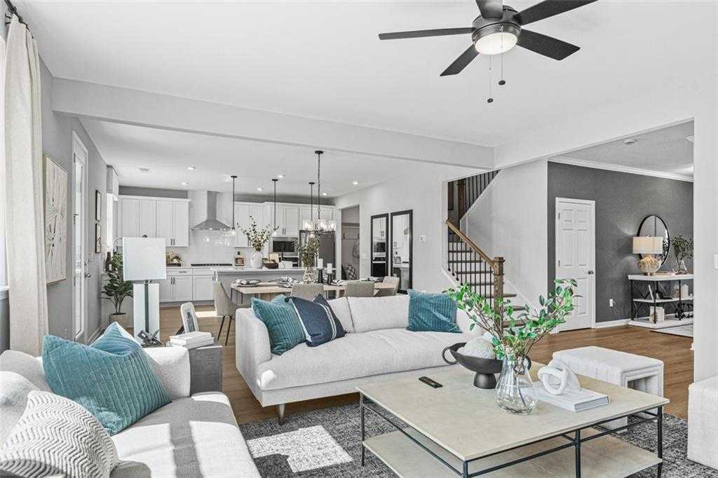 Open-concept living room with white sectional sofa, teal pillows, and modern kitchen in 5-bedroom Davidson Homes The Hickory B, Hoschton, GA