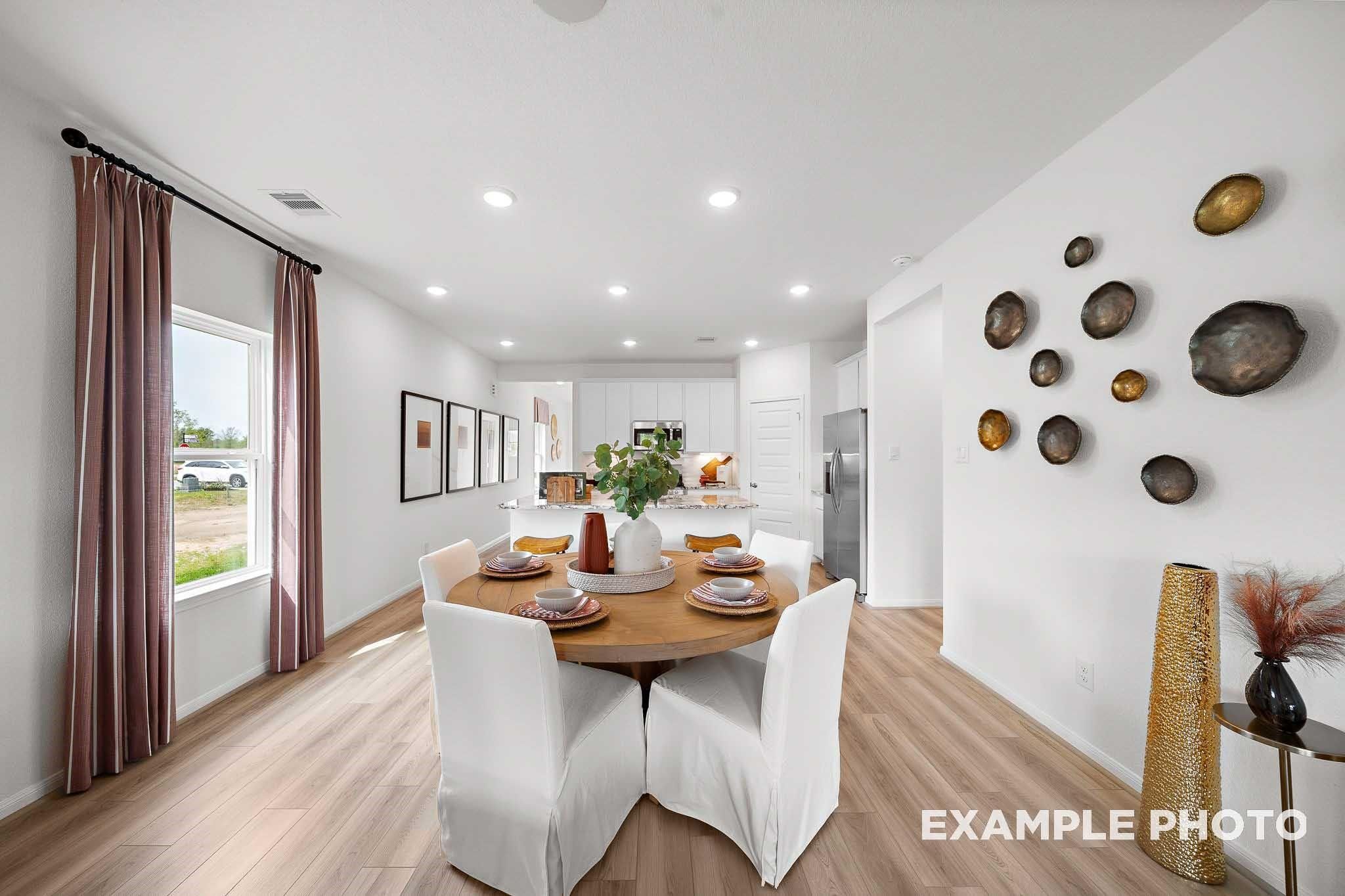 Open-concept dining area with round wooden table, white chairs, and modern white kitchen in Davidson Homes The Sabine F, Magnolia, Texas