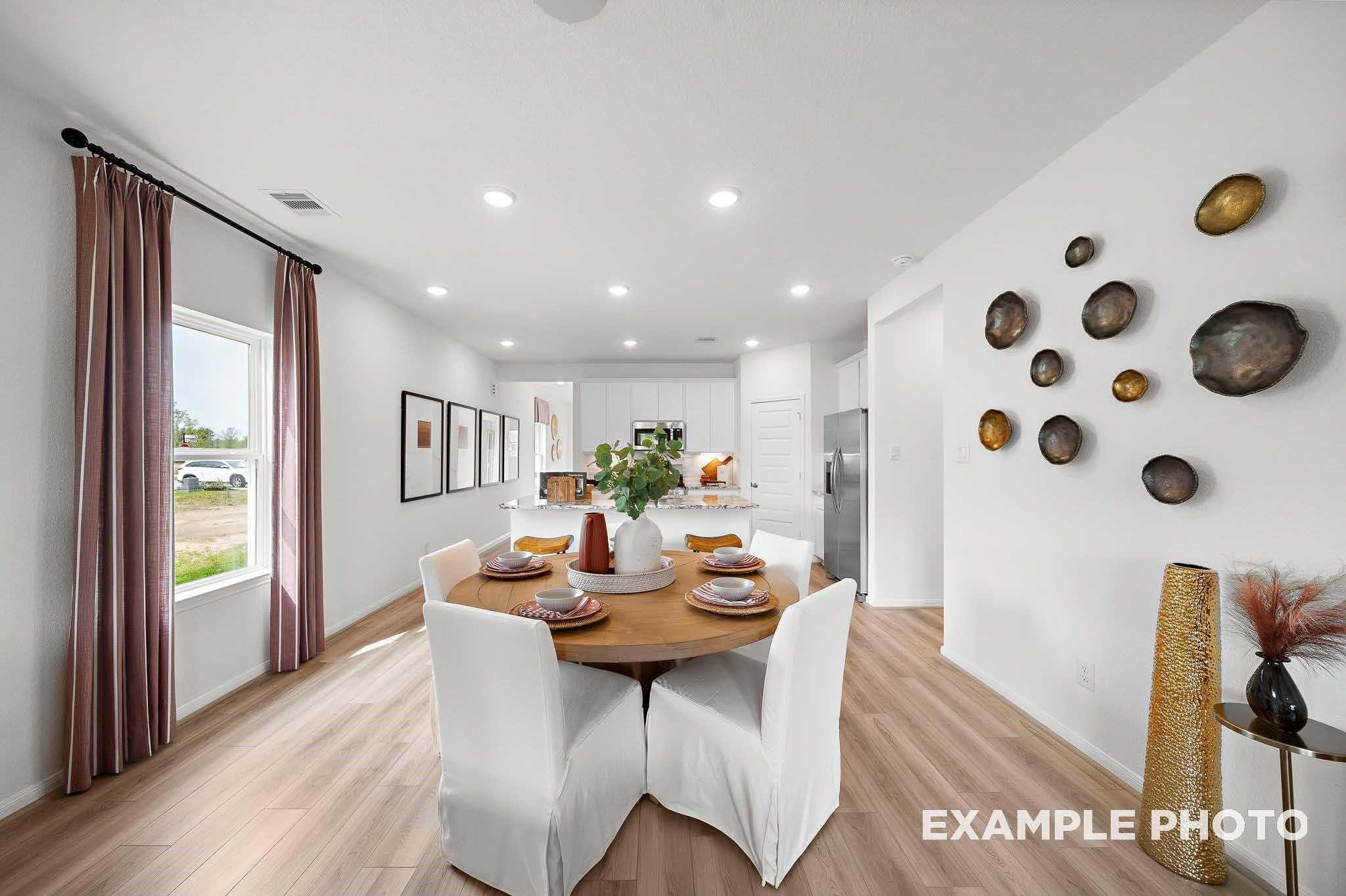 Open-concept dining area with round wooden table, white chairs, and modern white kitchen in Davidson Homes The Sabine F, Magnolia, Texas