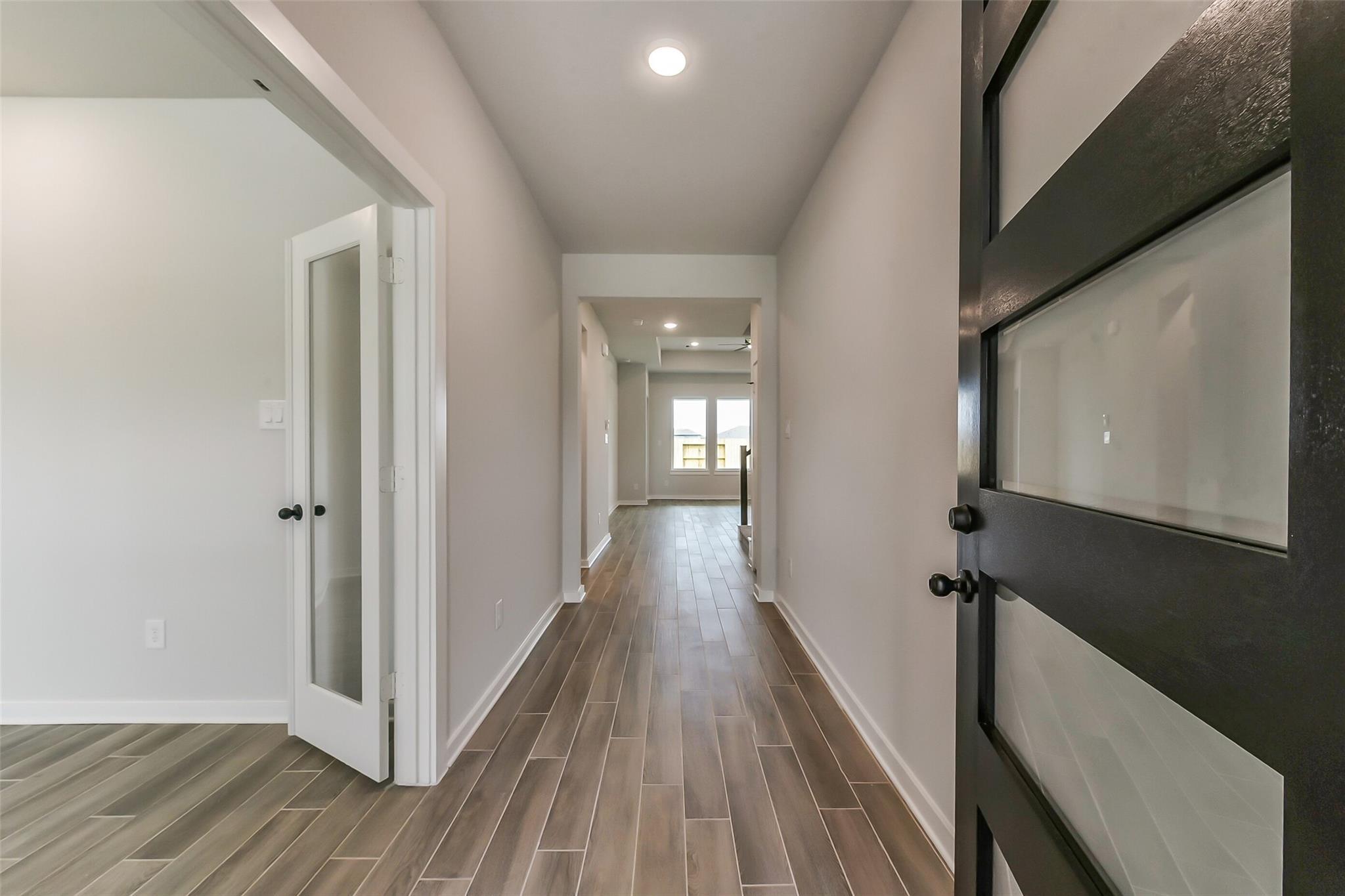 Elegant long hallway with wood-look tile flooring, recessed lights, and frosted glass doors in 4-bedroom Sequoia C home, Crosby, Texas
