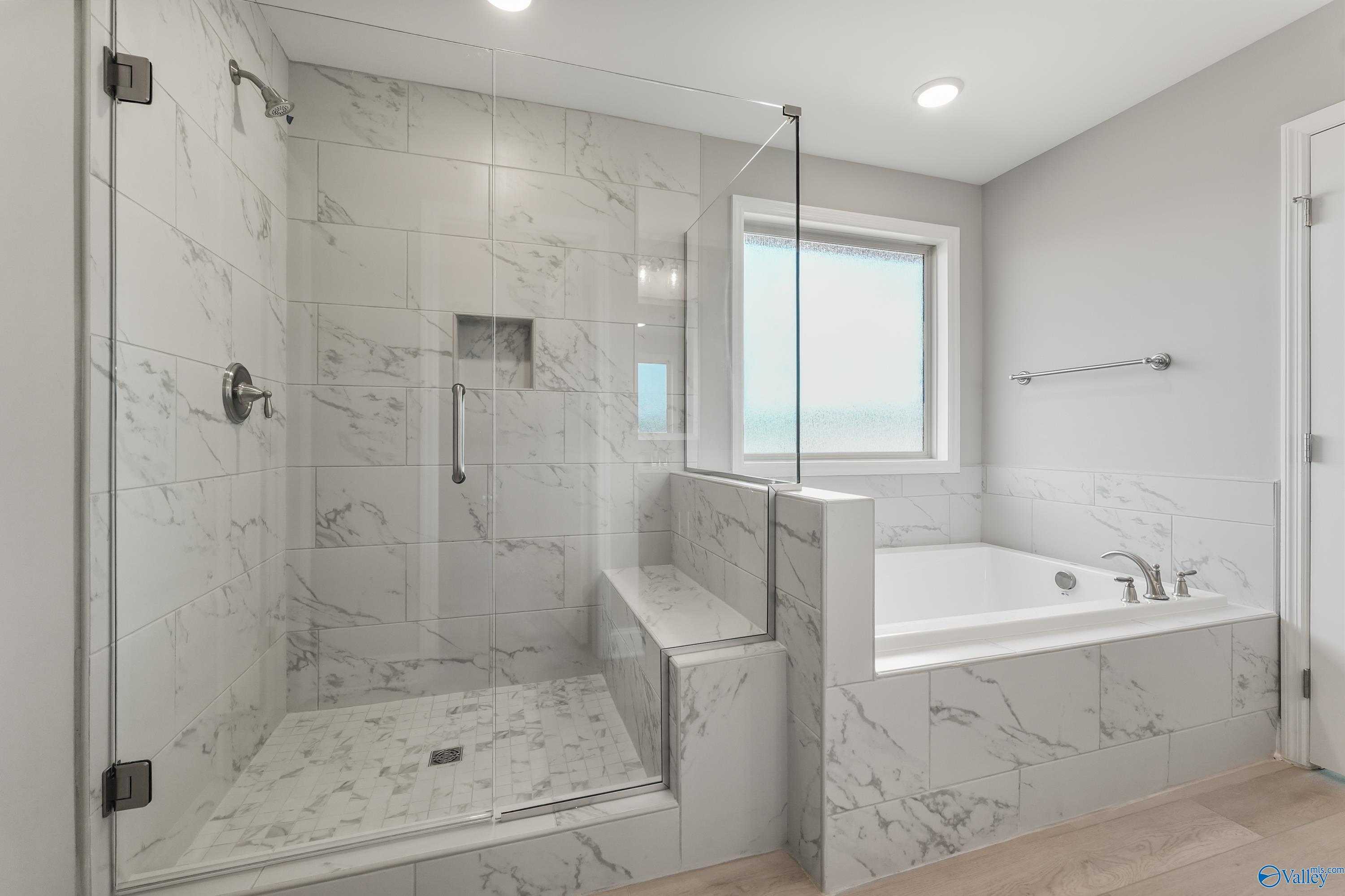 Elegant master bathroom featuring marble-tiled walk-in shower, freestanding tub, and large window in Davidson Homes The Everett B, Athens, AL