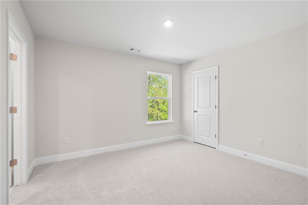 Bright secondary bedroom with light gray walls, beige carpet, and window overlooking trees in Davidson Homes The Hickory E, Buford, GA