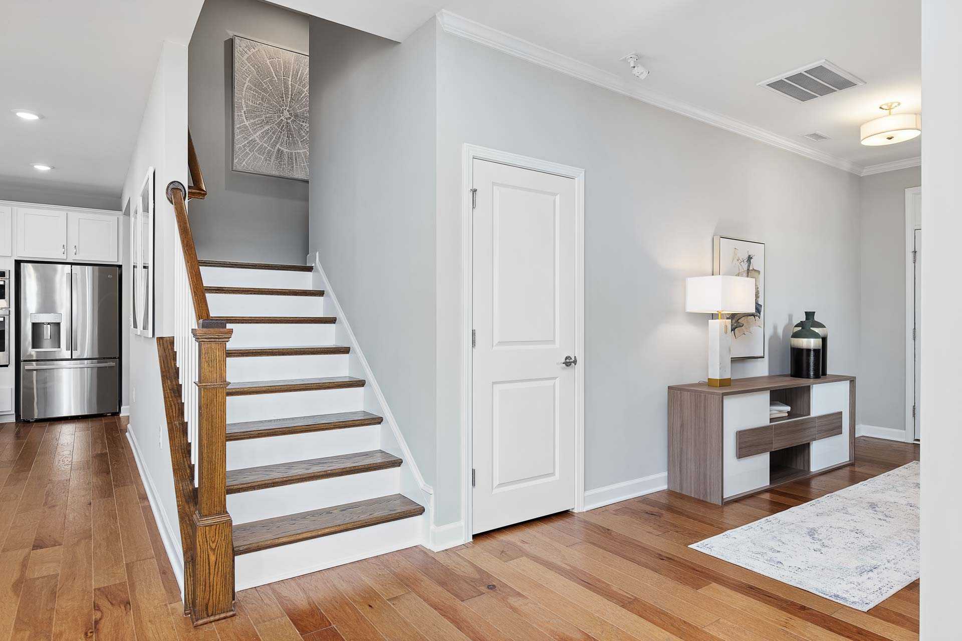 Modern home interior with oak staircase, hardwood floors, and white kitchen at Highland Forest in Fuquay-Varina, NC