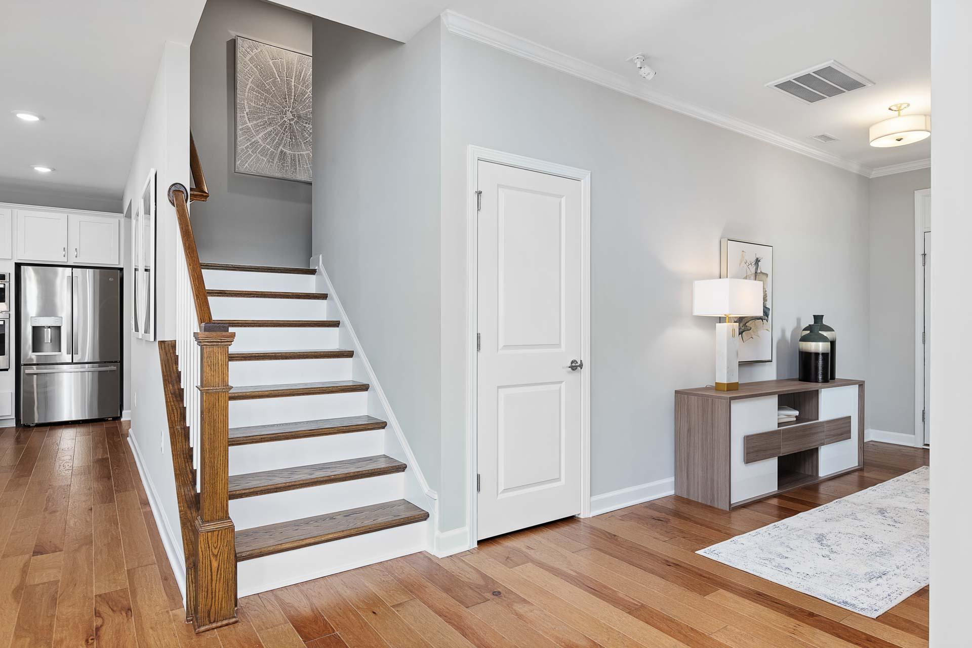 Modern home interior with oak staircase, hardwood floors, and white kitchen at Highland Forest in Fuquay-Varina, NC