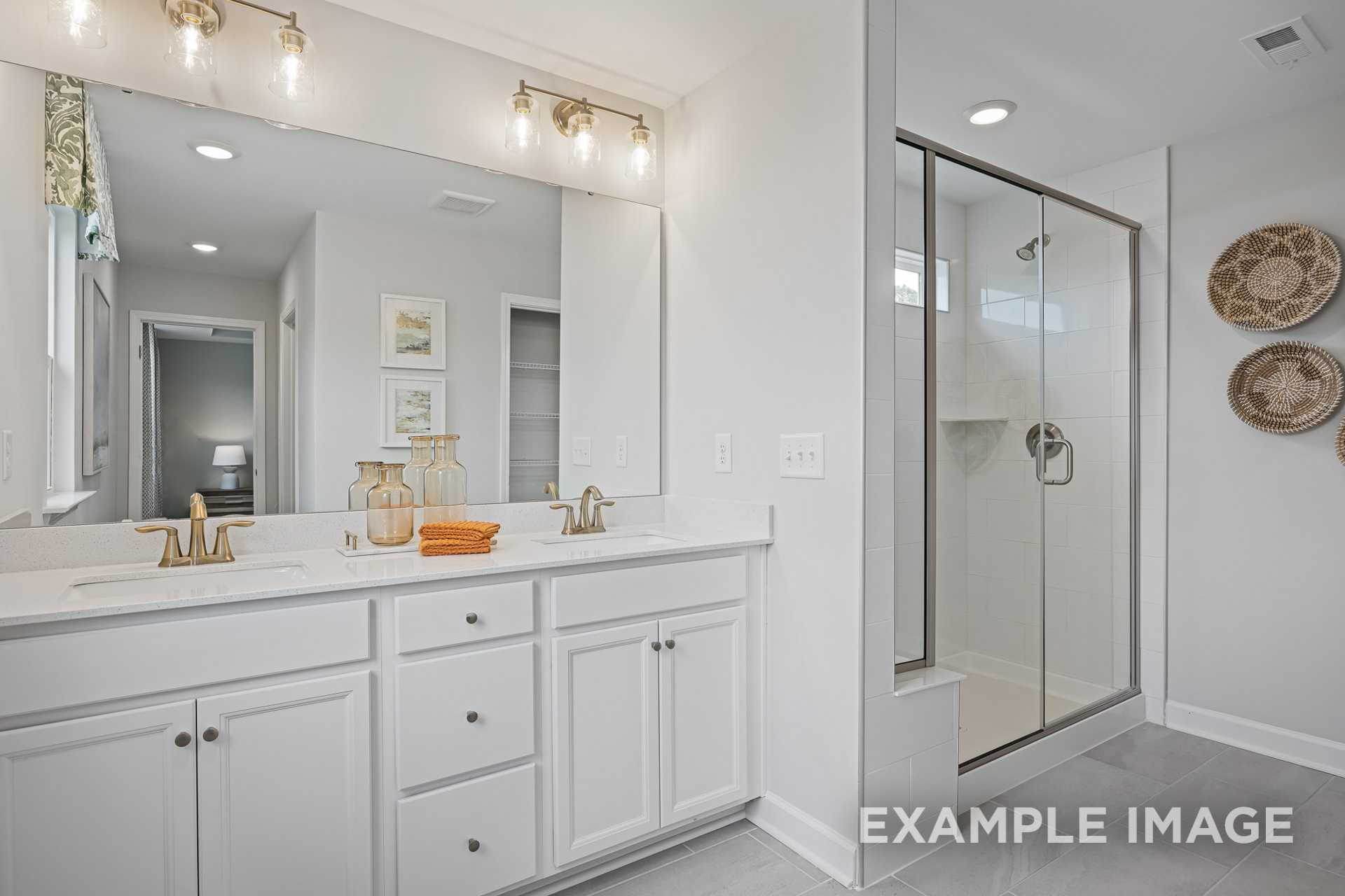 Spacious master bathroom in The Adalynn A with white double vanity, large mirror, and frameless glass shower